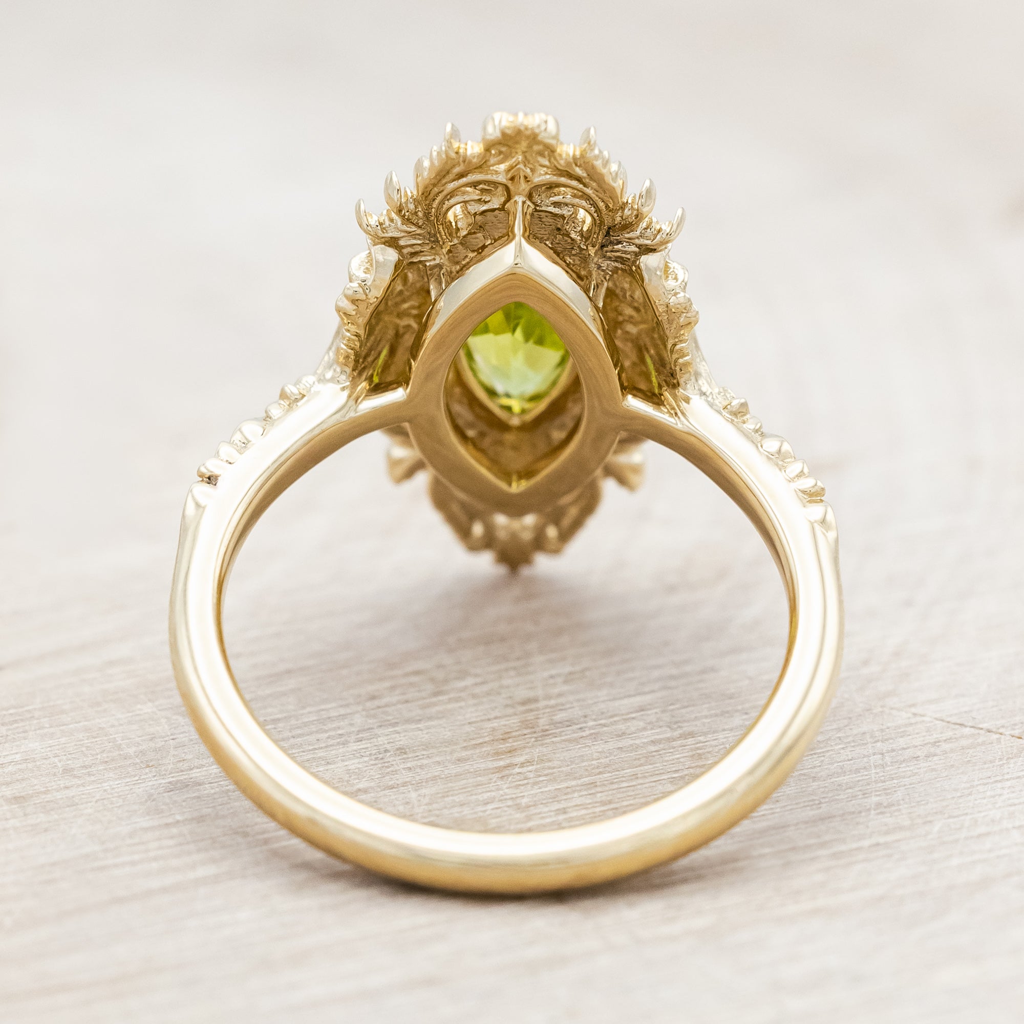 Yellow gold ring with a green peridot on a beige background