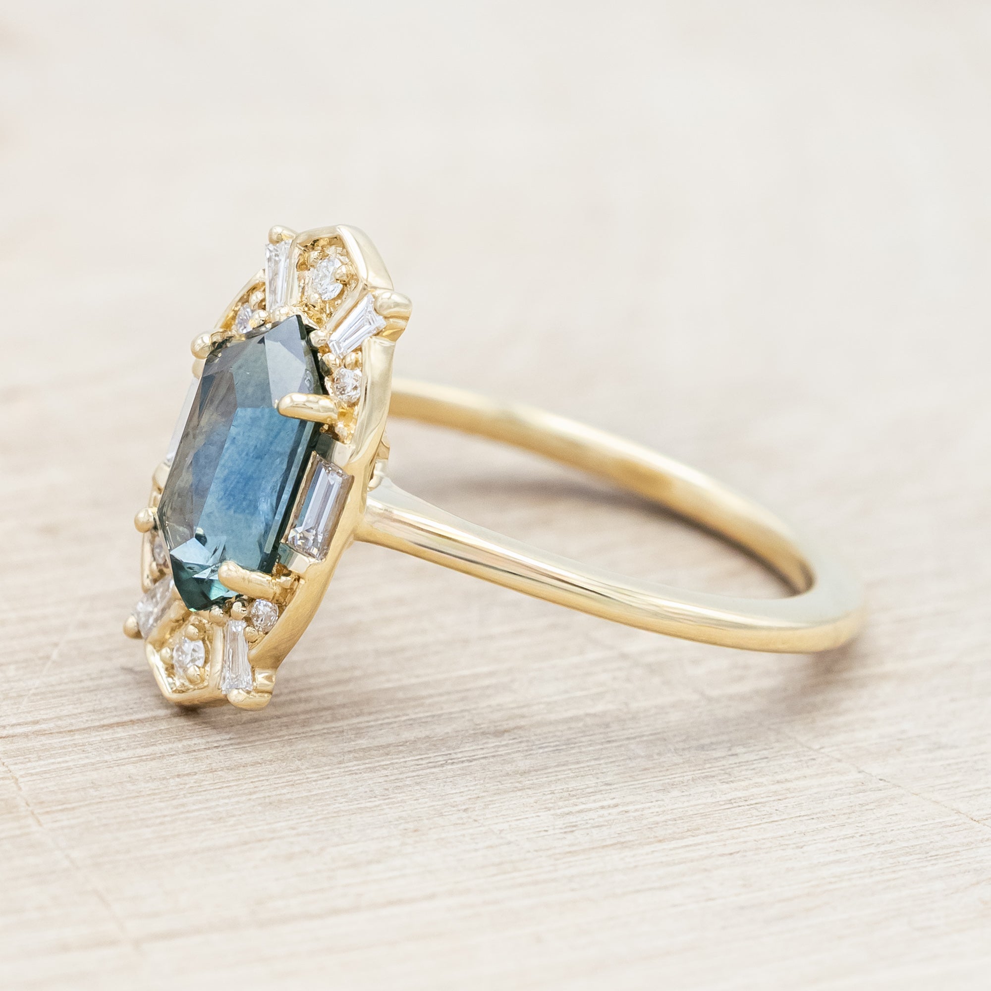 14K gold ring with Montana sapphire and diamond accents on a beige background