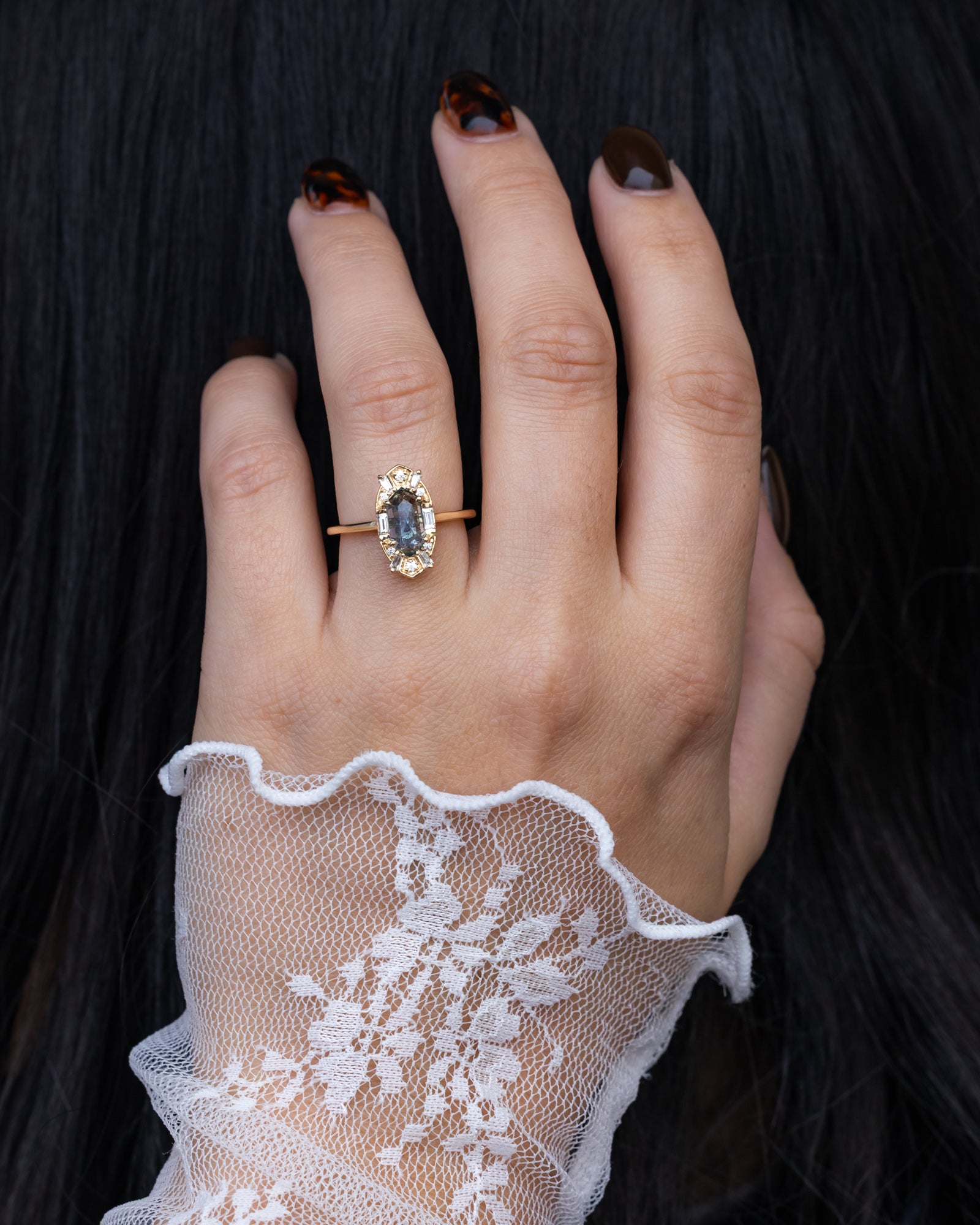 Hand wearing a ring with a Montana sapphire against a dark background