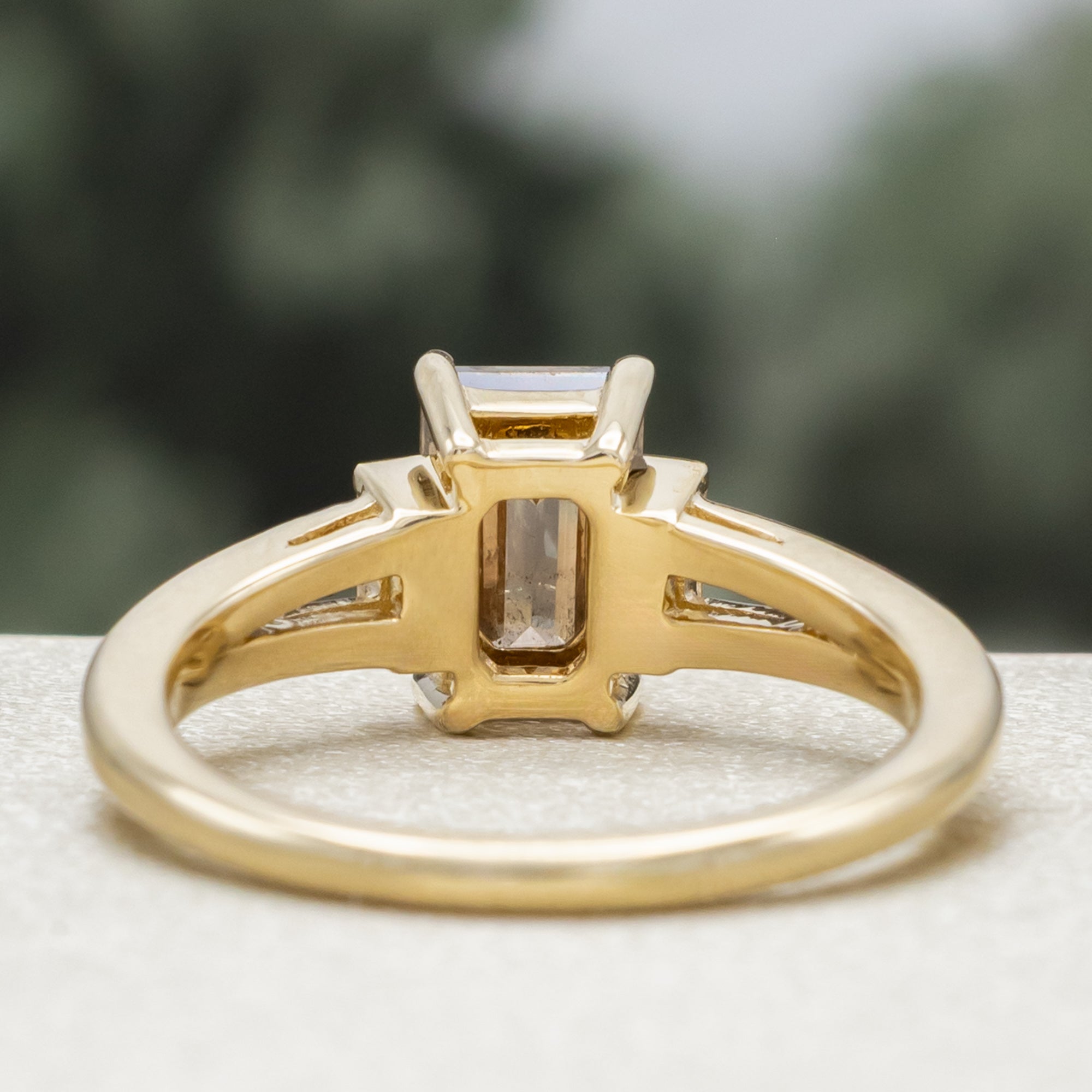 Gold ring with champagne diamond centerstone & diamond accent against a blurred green background