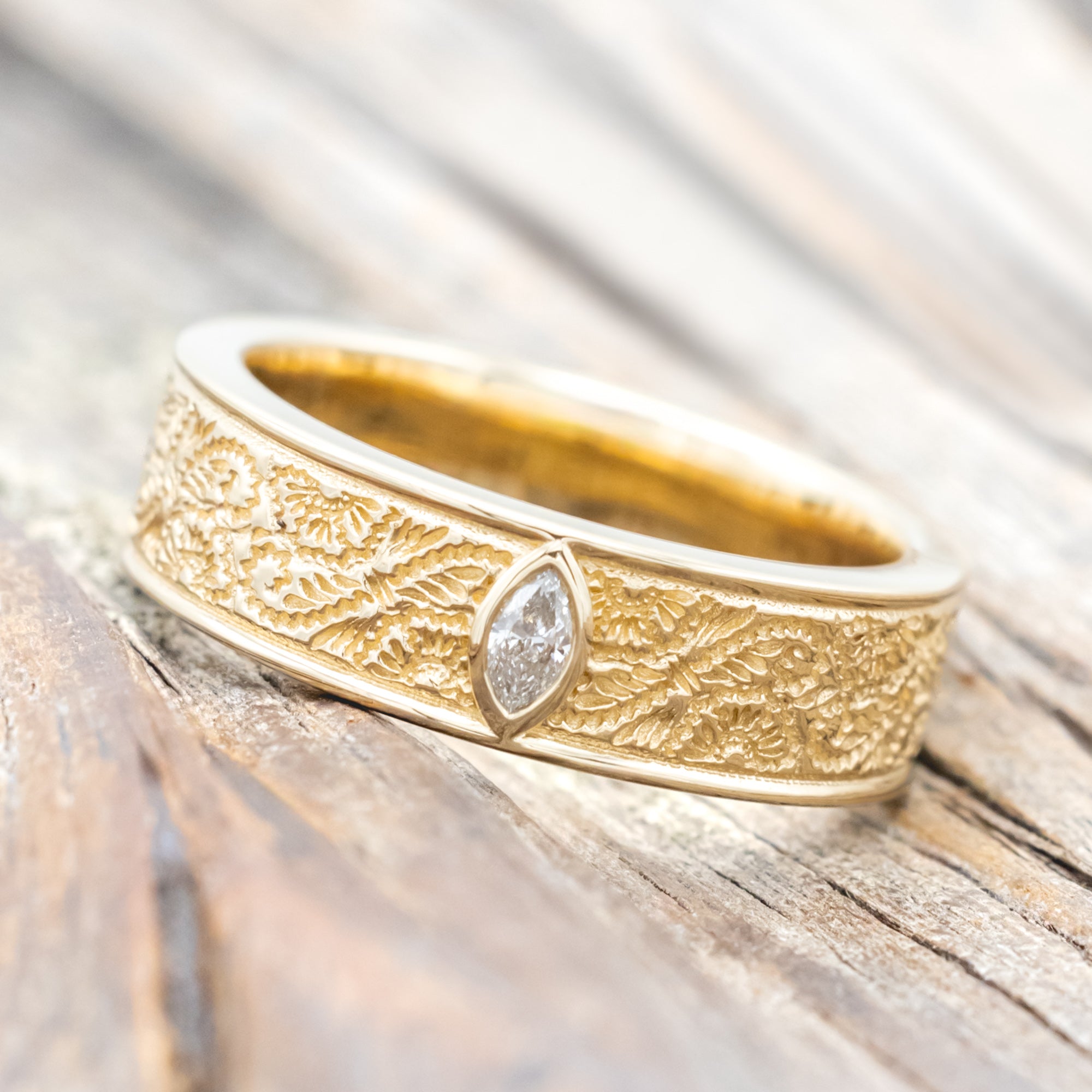 Yellow gold ring with floral engravings and diamond accent on wooden surface