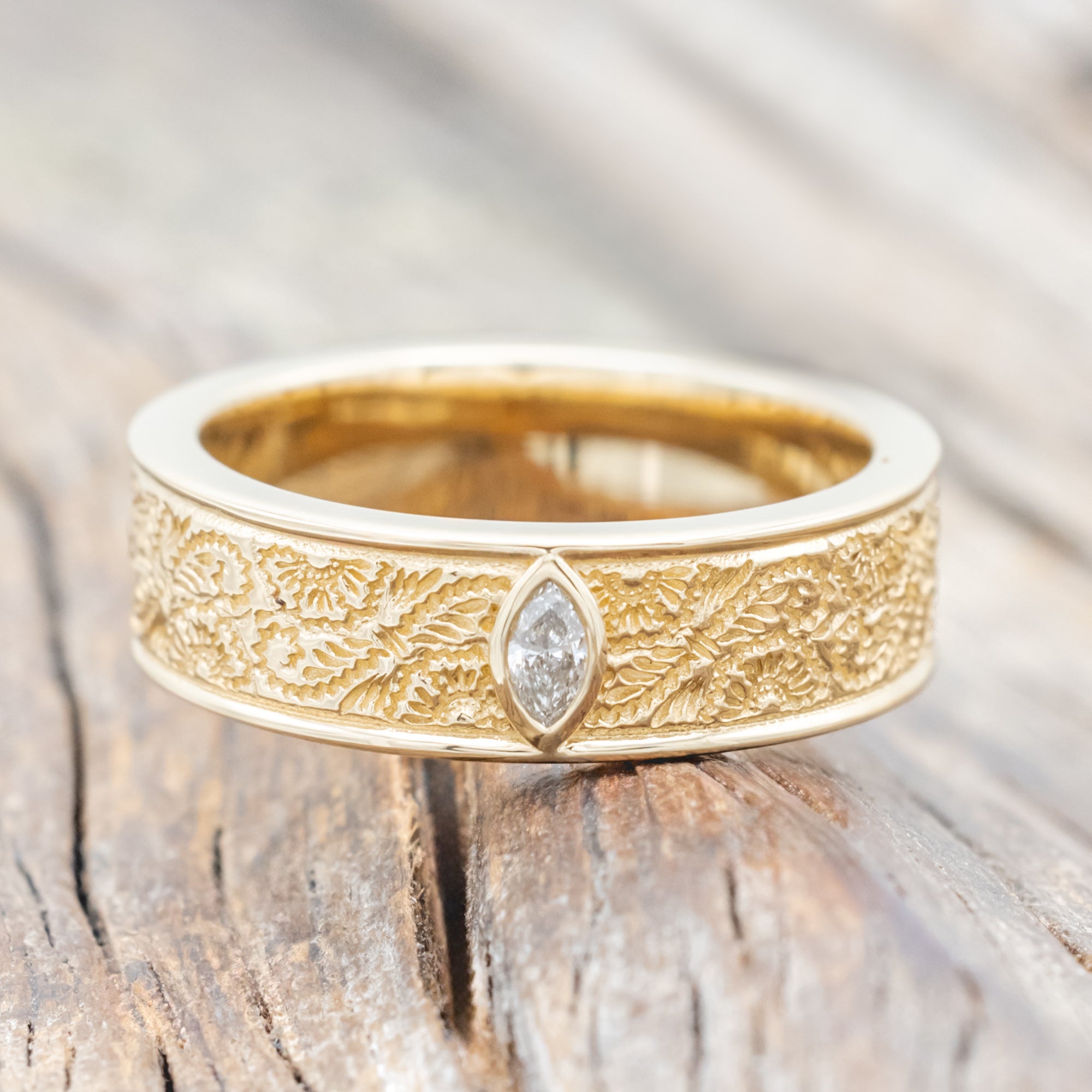 Yellow gold ring with floral engravings and diamond accent on wooden surface