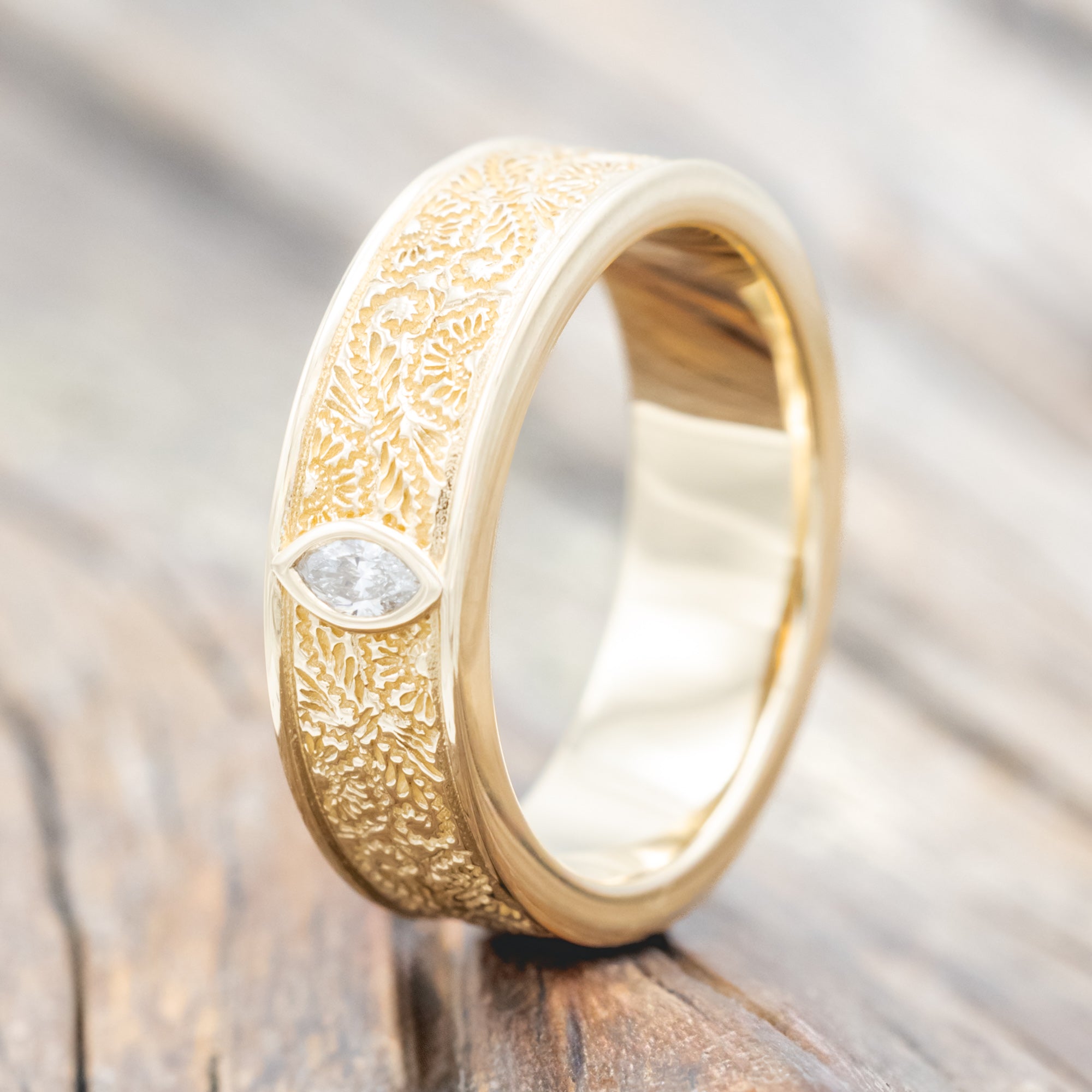 Yellow gold ring with floral engravings and diamond accent on wooden surface