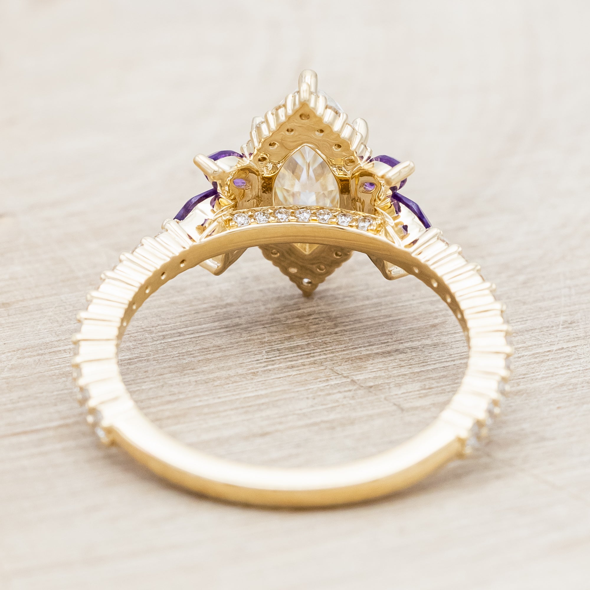 Yellow gold ring with a moissanite center stone and small purple amethyst accents on a beige background