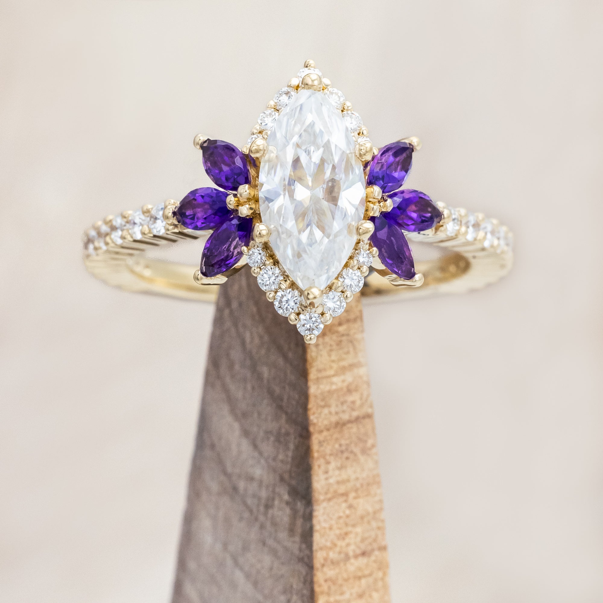 Yellow gold ring with a moissanite center stone and small purple amethyst accents on a beige background