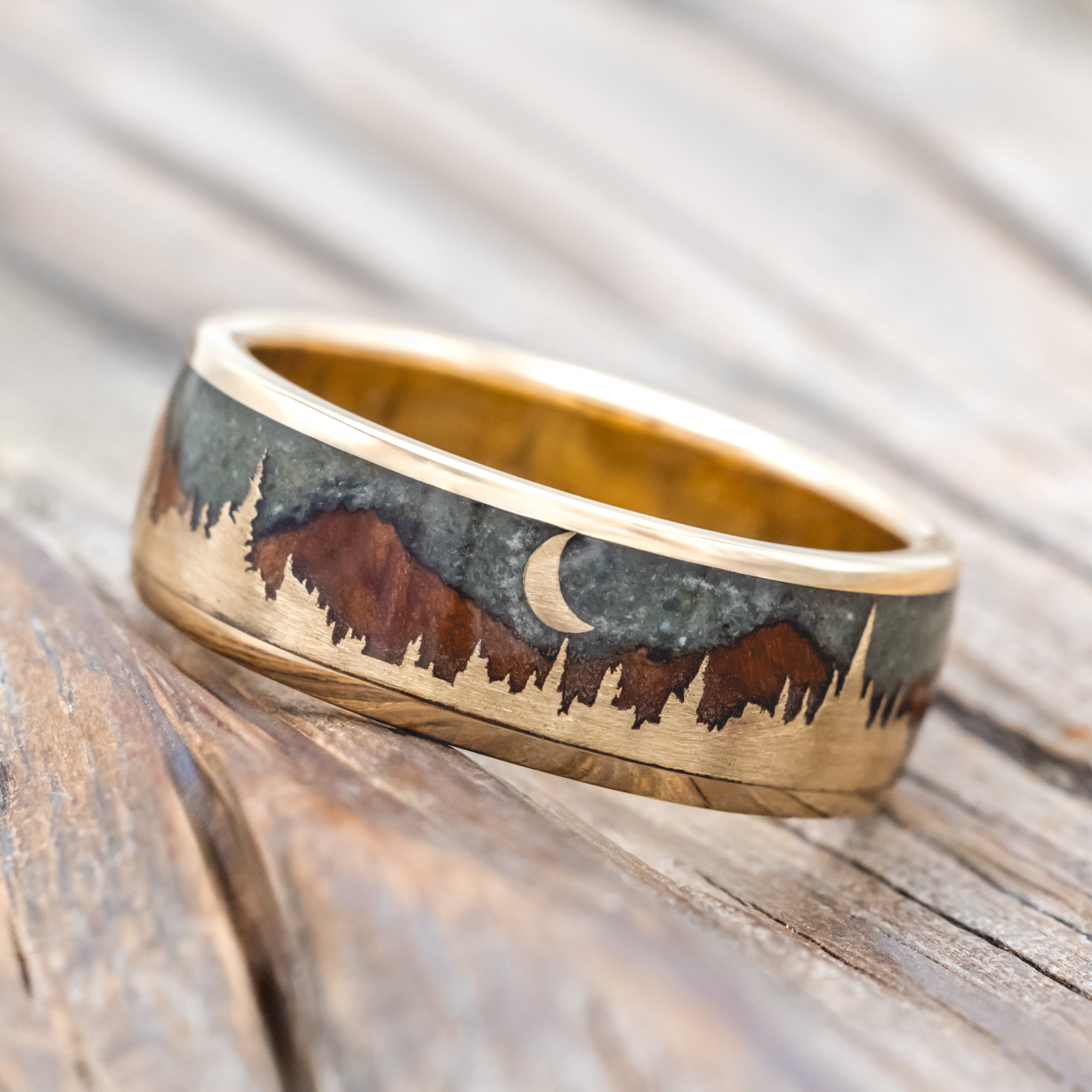 Ring with engraved design of mountains and a moon on a wooden surface