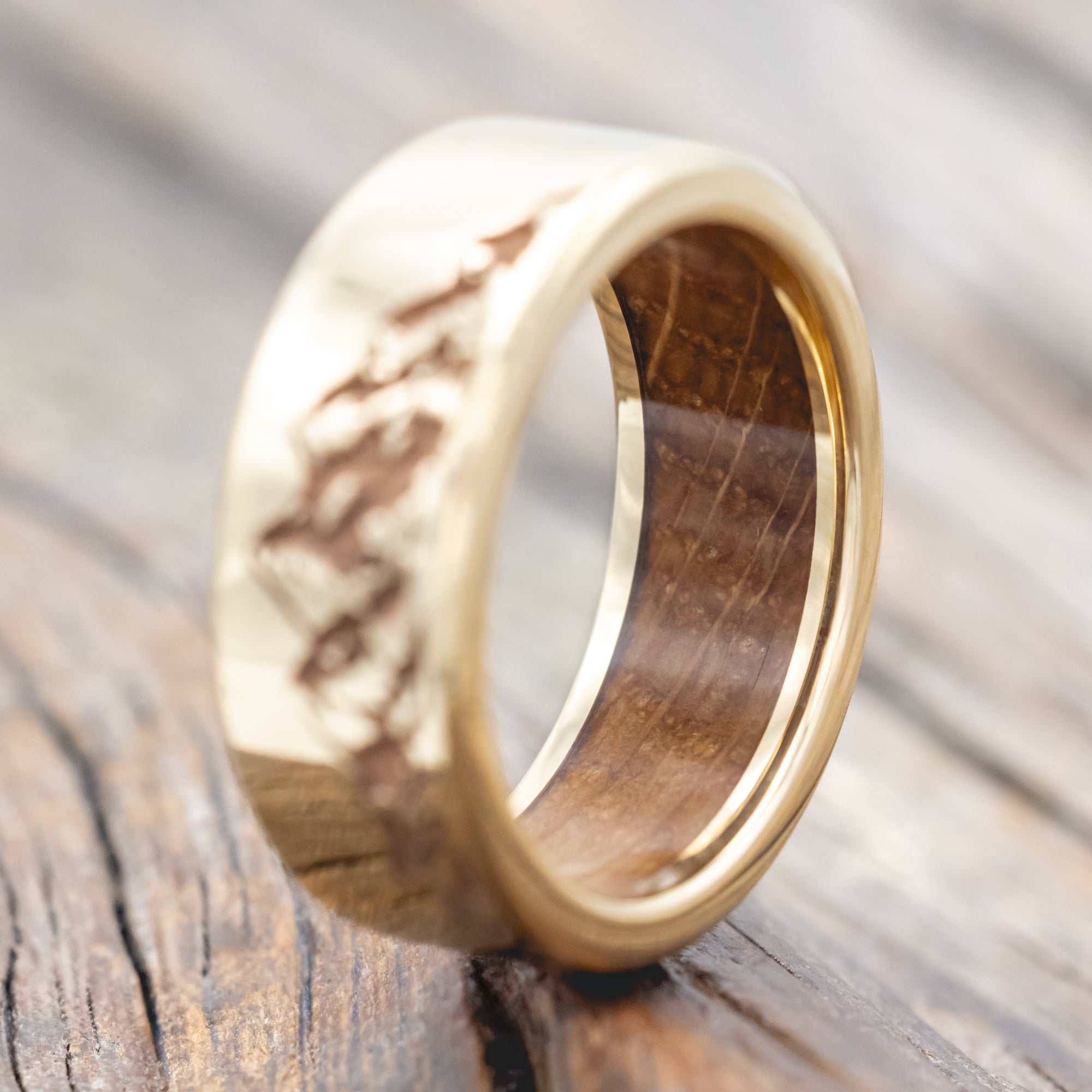 Gold ring with mountain engraving and whiskey barrel lining on a wooden surface