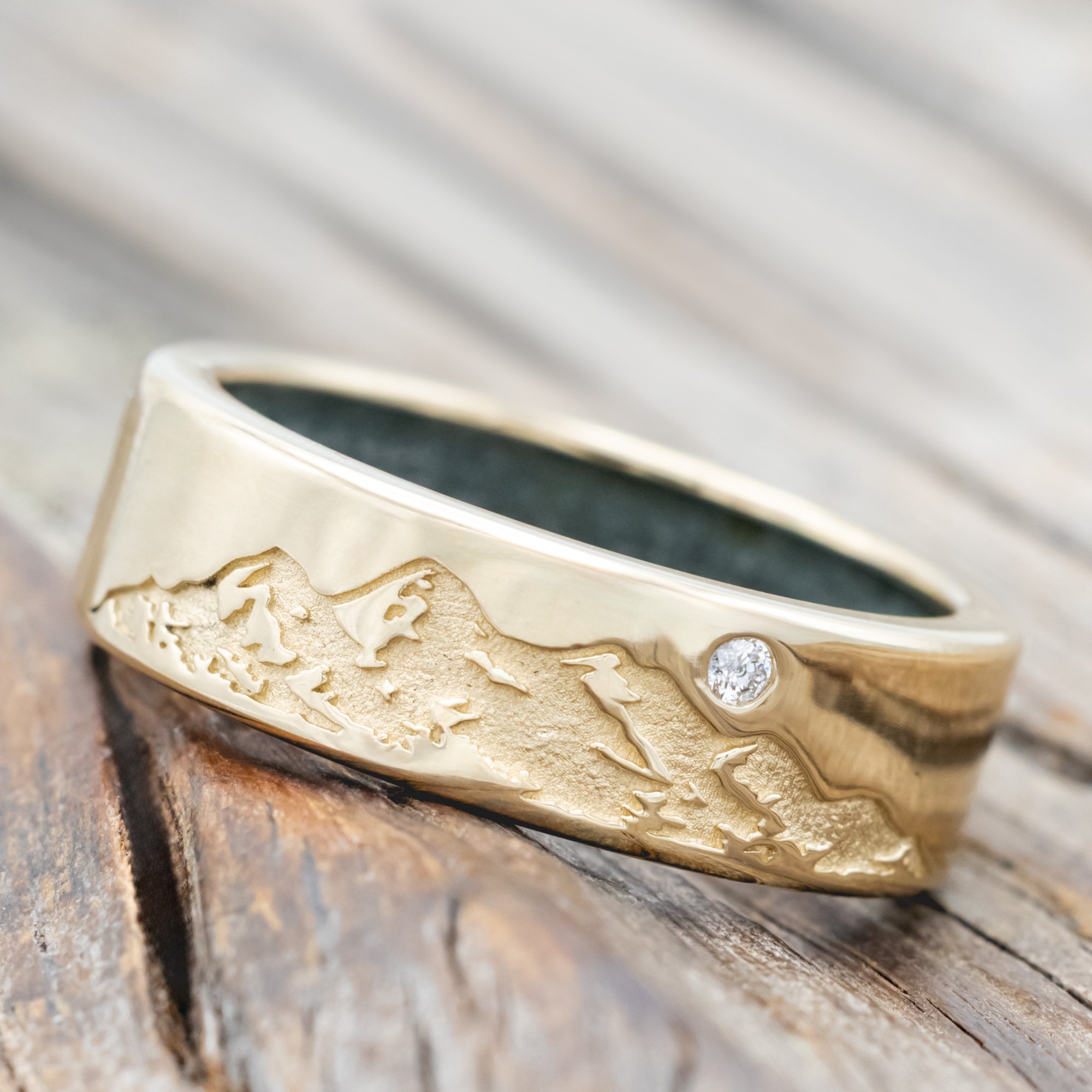 Gold ring with moss agate lining, diamond accent & mountain engraving on a wooden surface