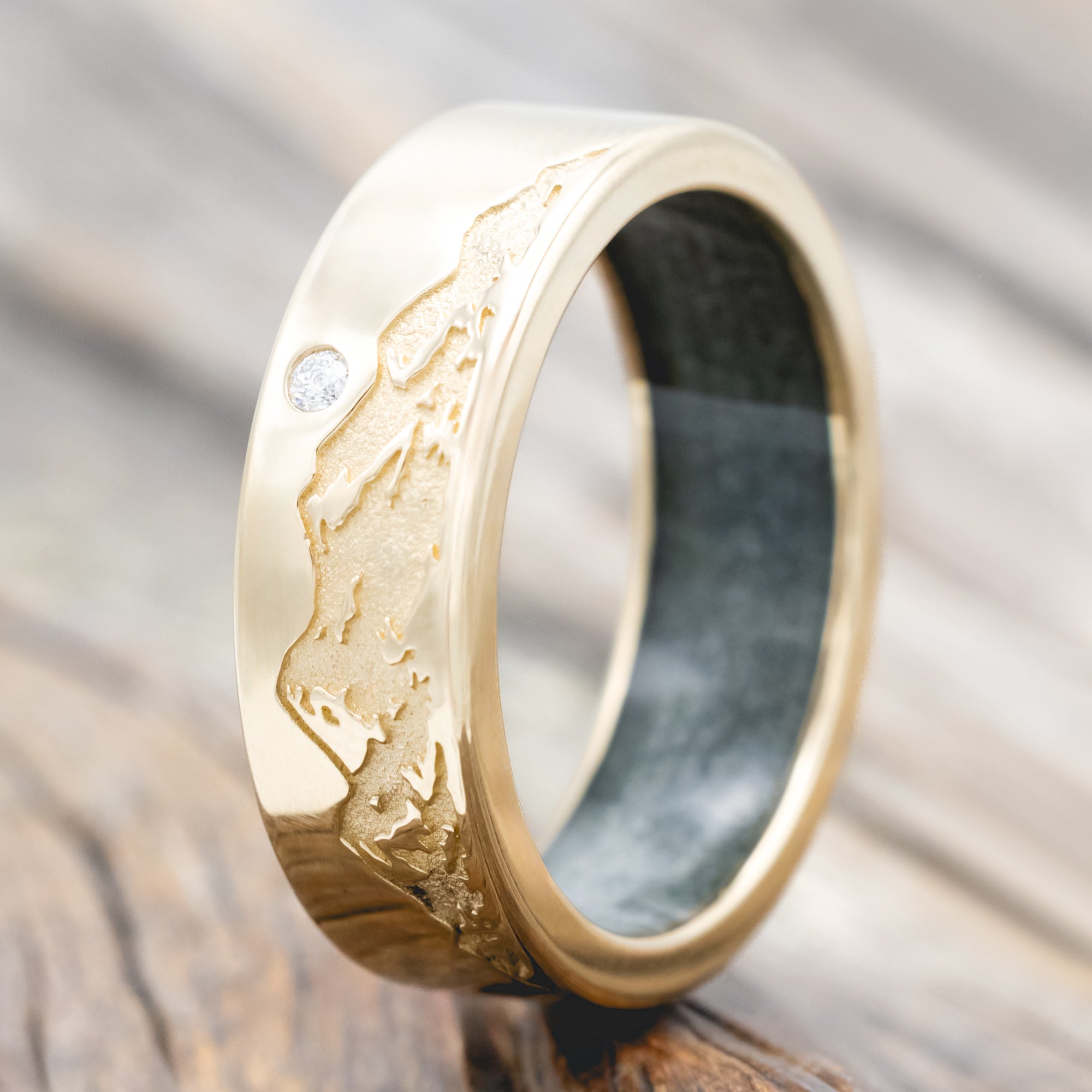 Gold ring with moss agate lining, diamond accent & mountain engraving on a wooden surface