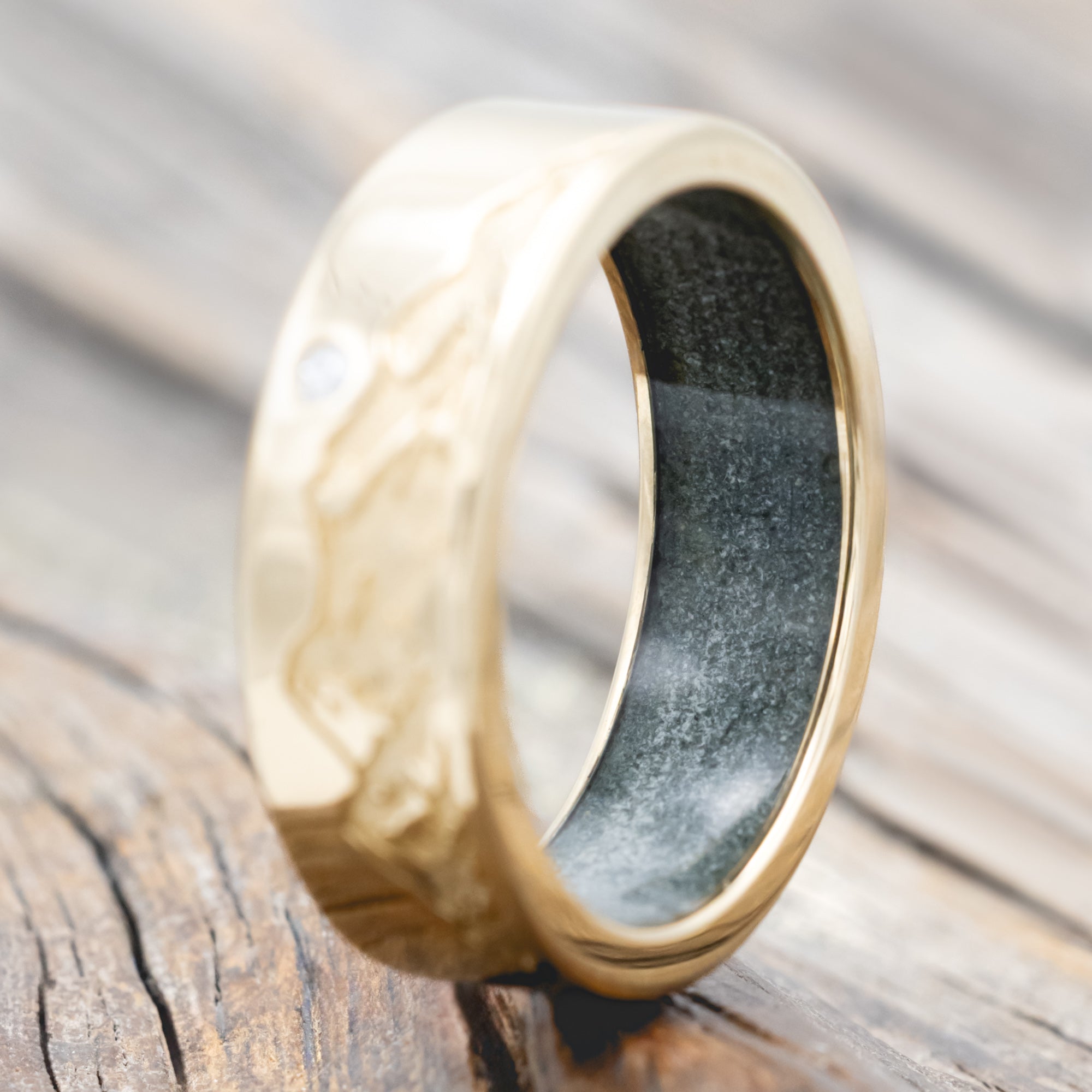 Gold ring with moss agate lining, diamond accent & mountain engraving on a wooden surface