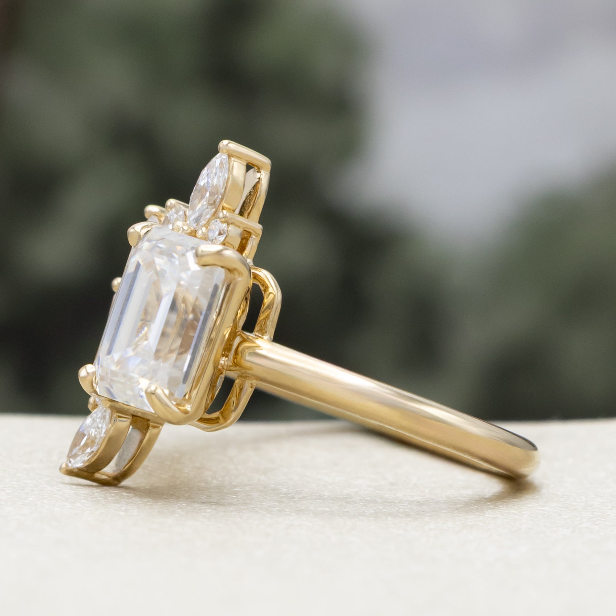 Gold ring with emerald-cut lab diamond and marquise diamond accents on a natural background