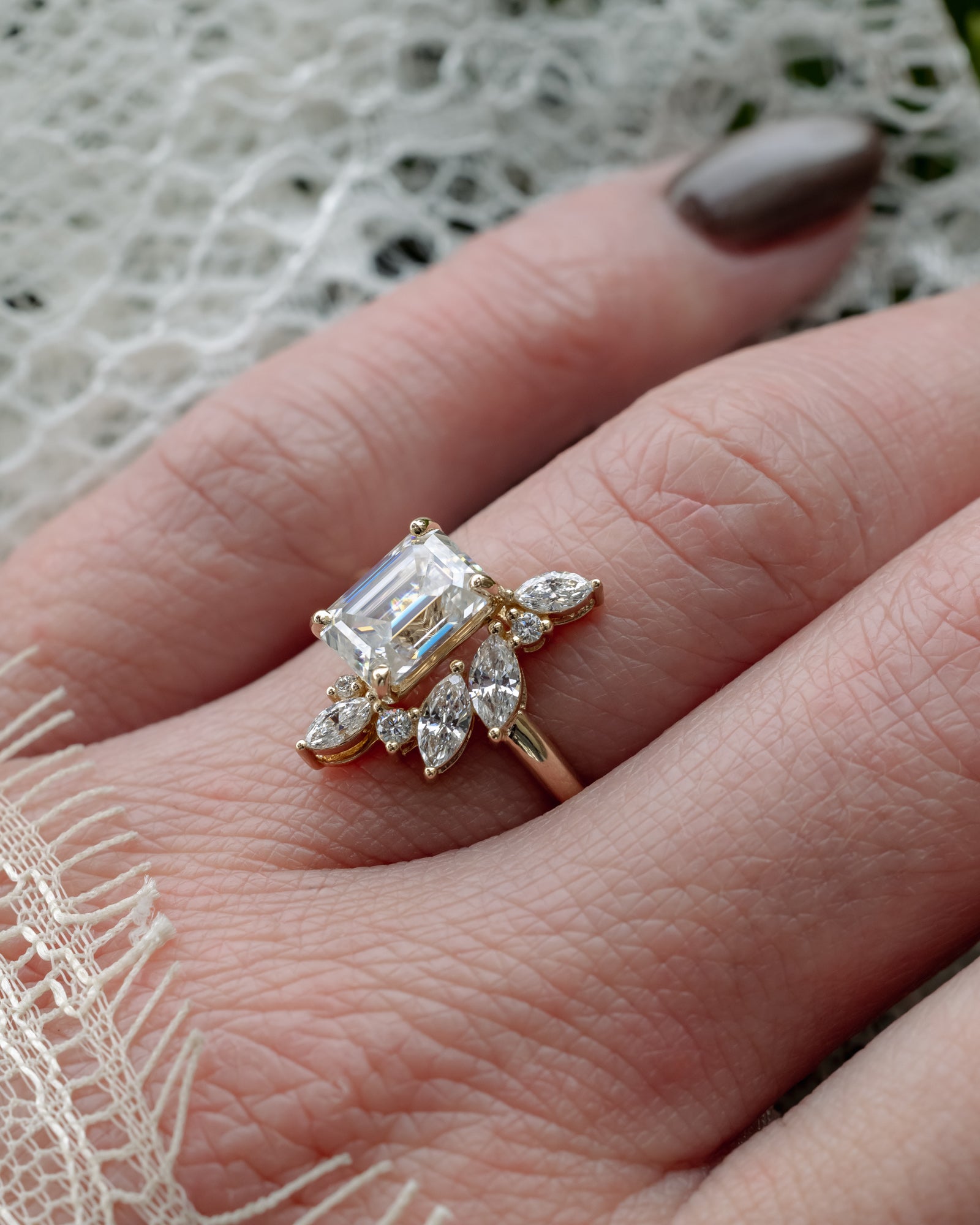 Gold ring with a lab diamond center stone and diamond accents on a hand against a textured background