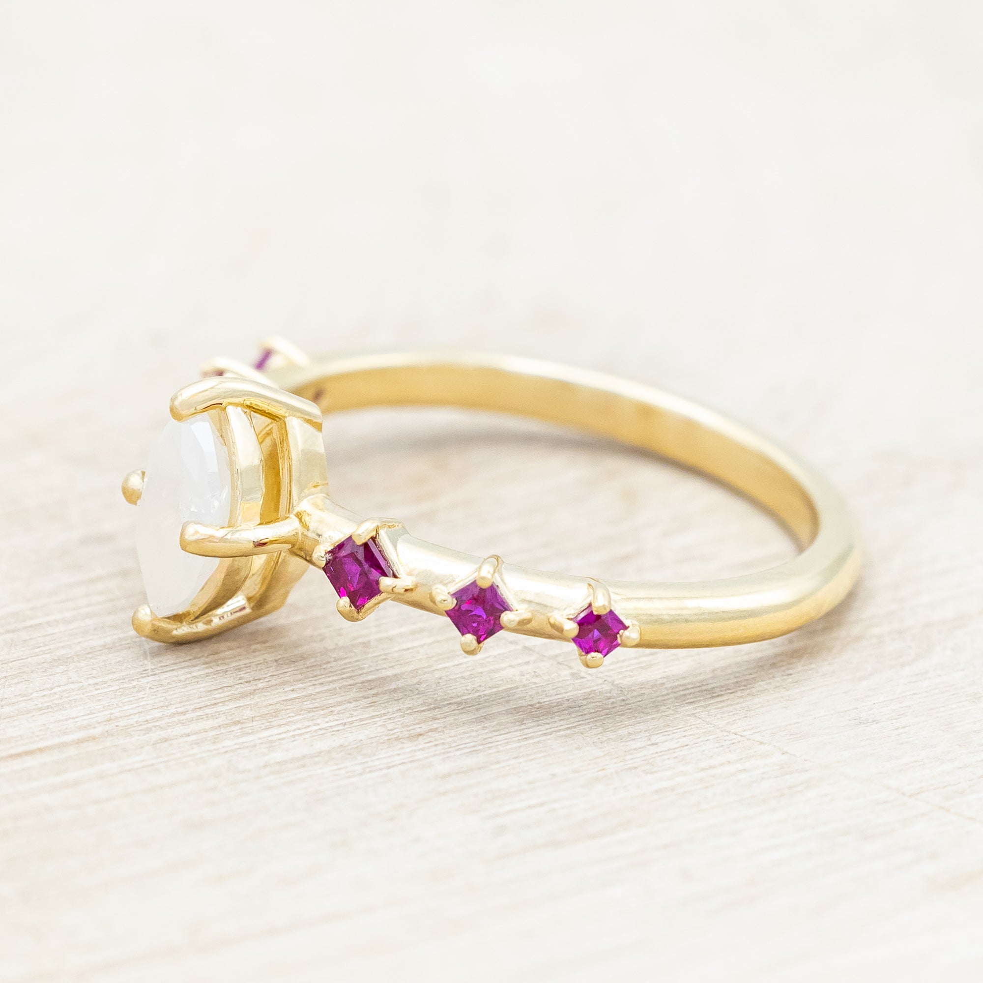 Gold ring with a central icy salt & pepper diamond with ruby accents on a beige background