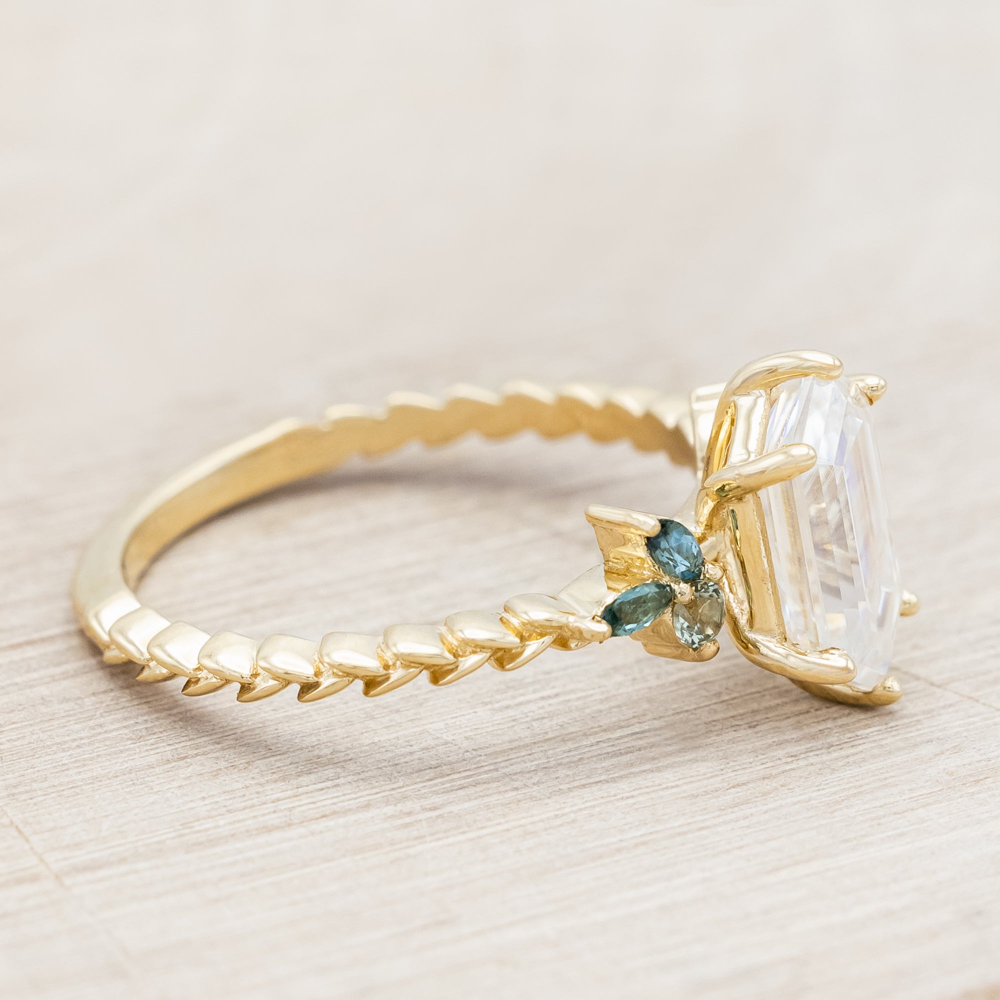 Gold ring with hexagon-cut diamond and green gemstone accents on a beige background