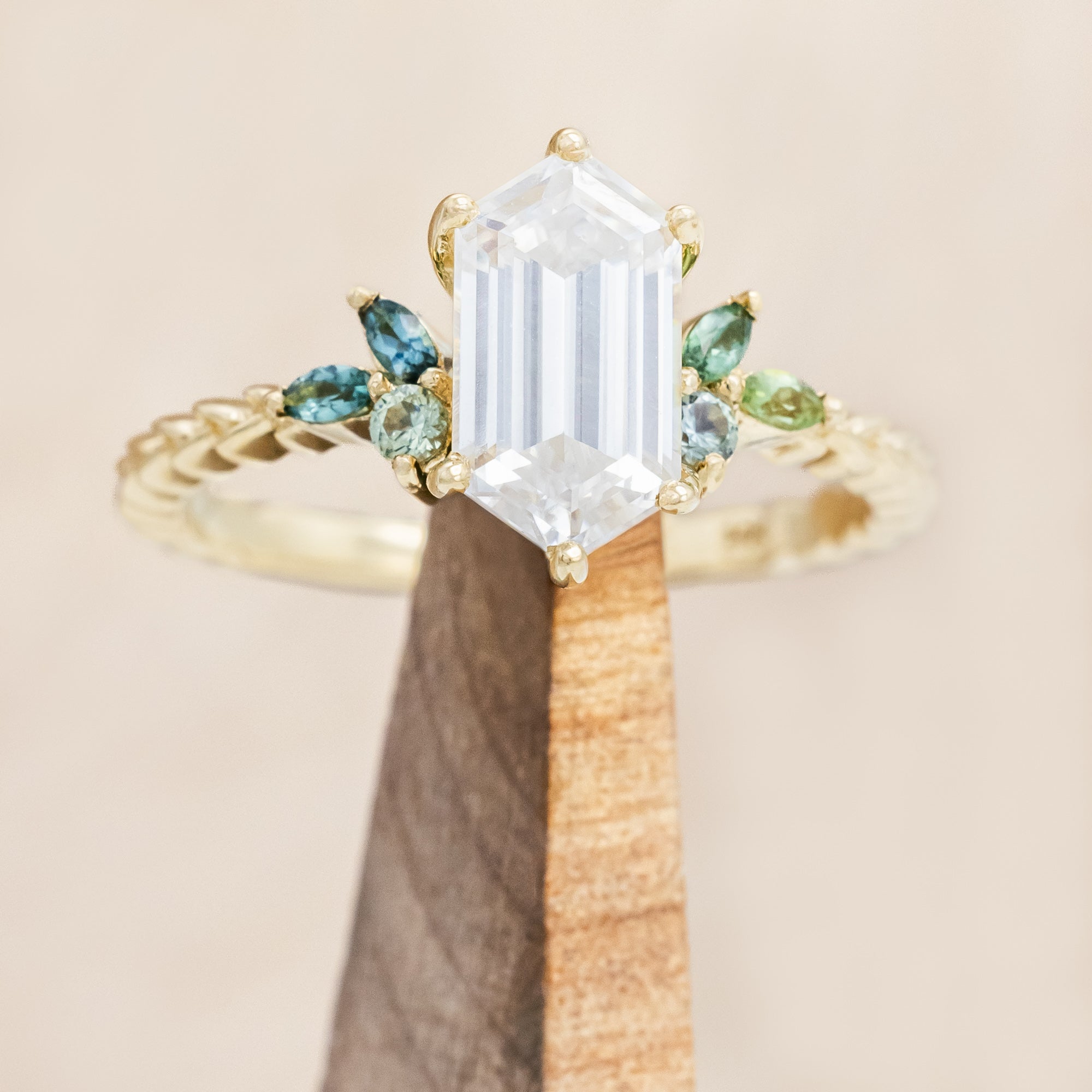 Gold ring with hexagon-cut diamond and green gemstone accents on a beige background