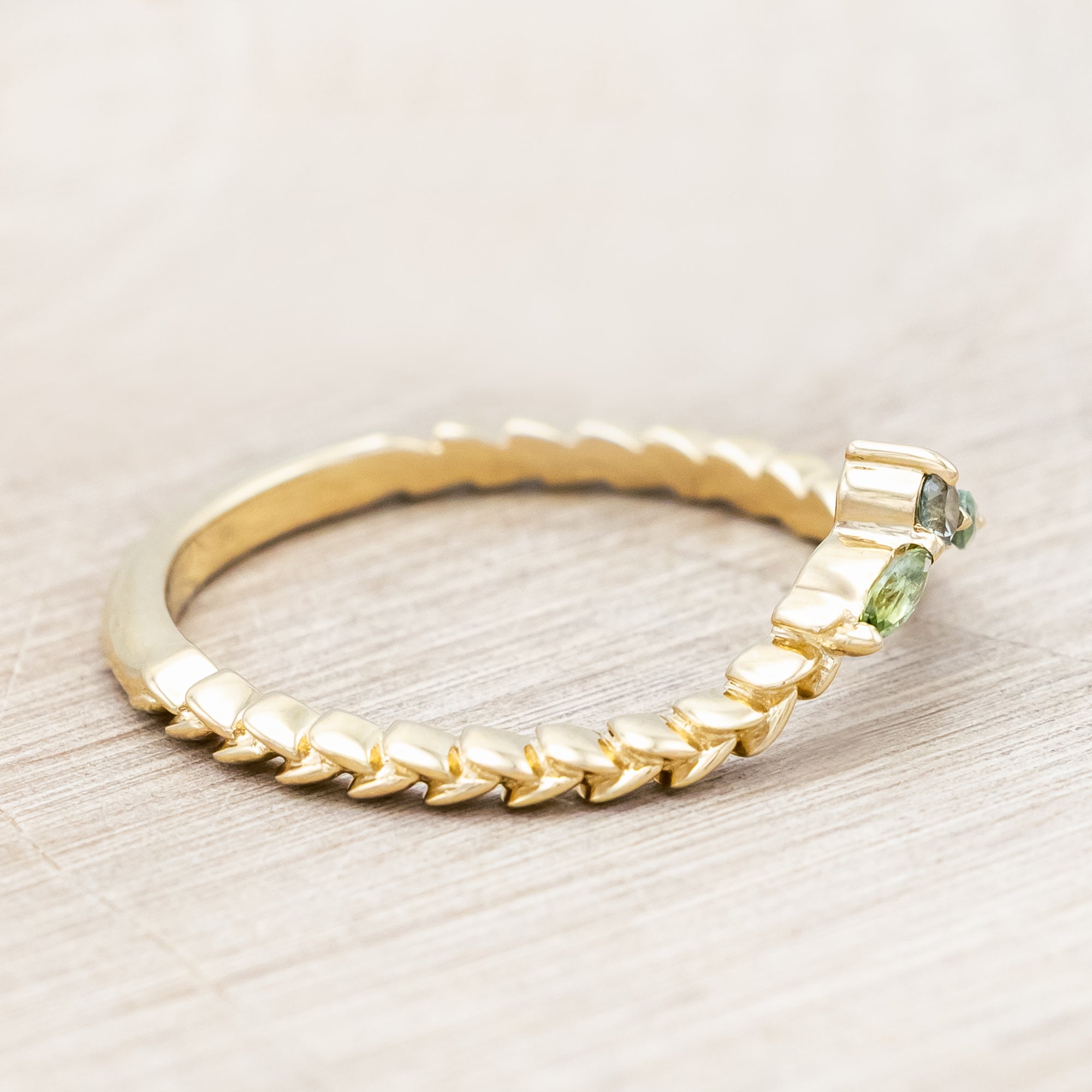 Gold ring with sapphire and tourmaline accents against a beige background