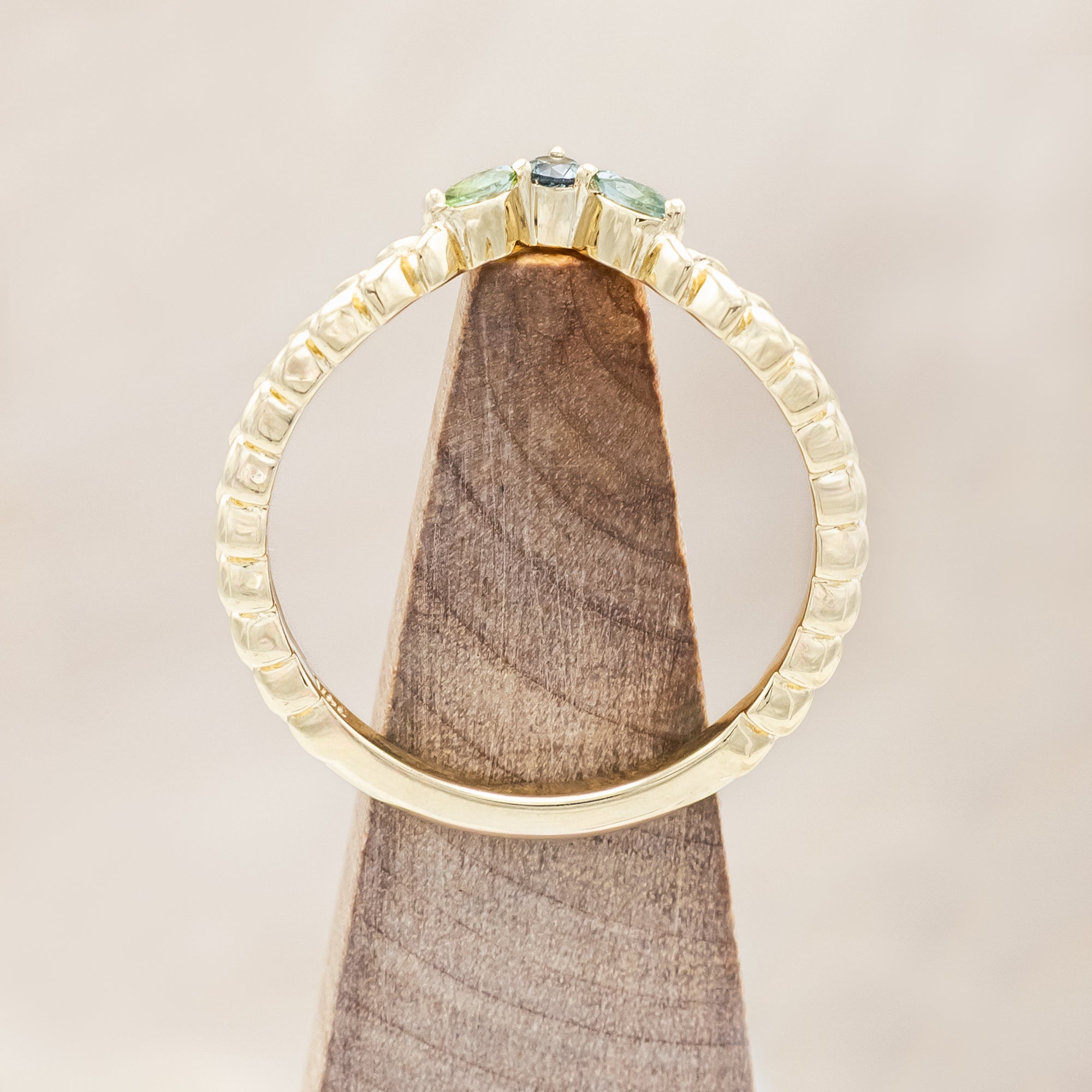 Gold ring with sapphire and tourmaline accents on a wooden stand against a beige background