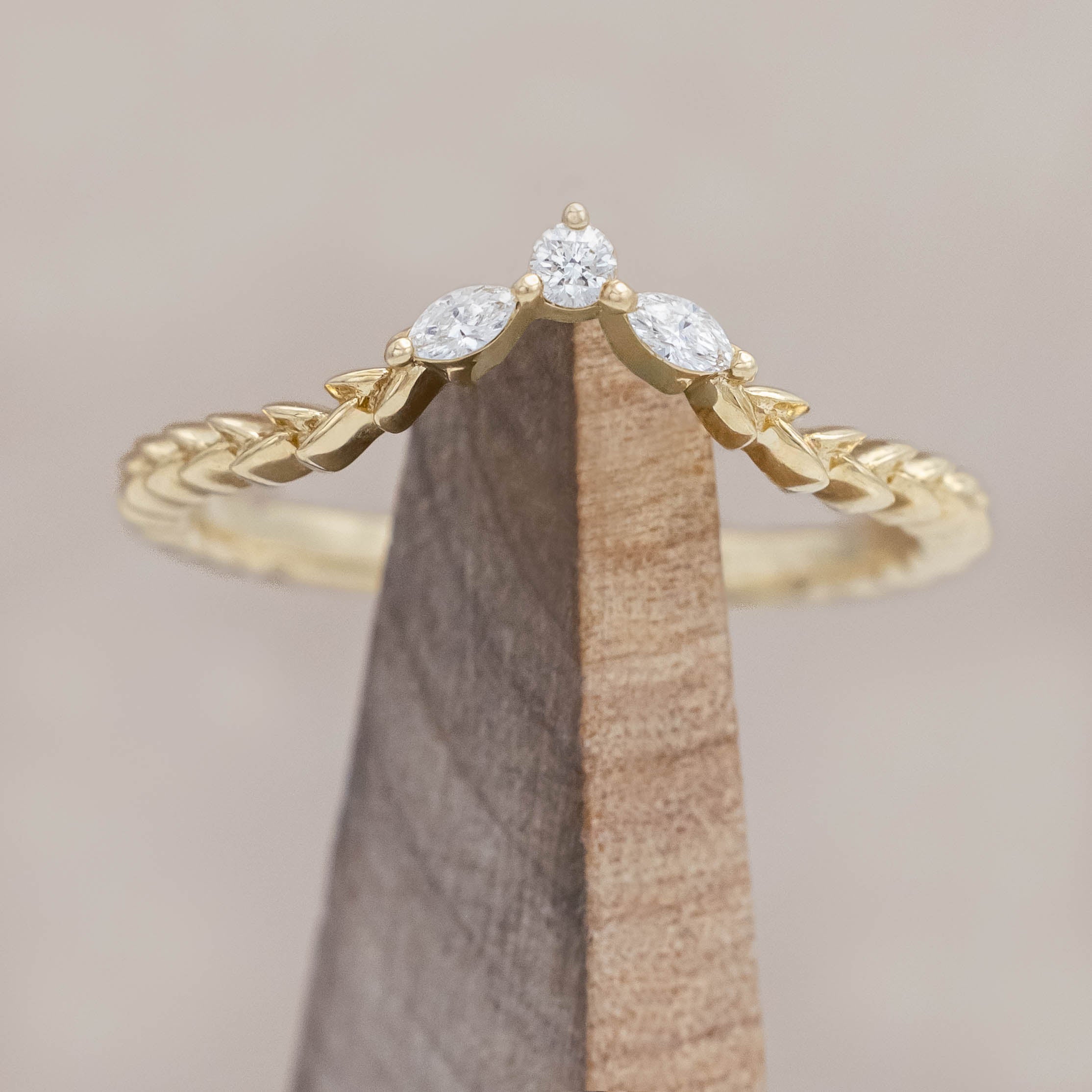 14K gold ring with three diamonds on a wooden stand against a beige background
