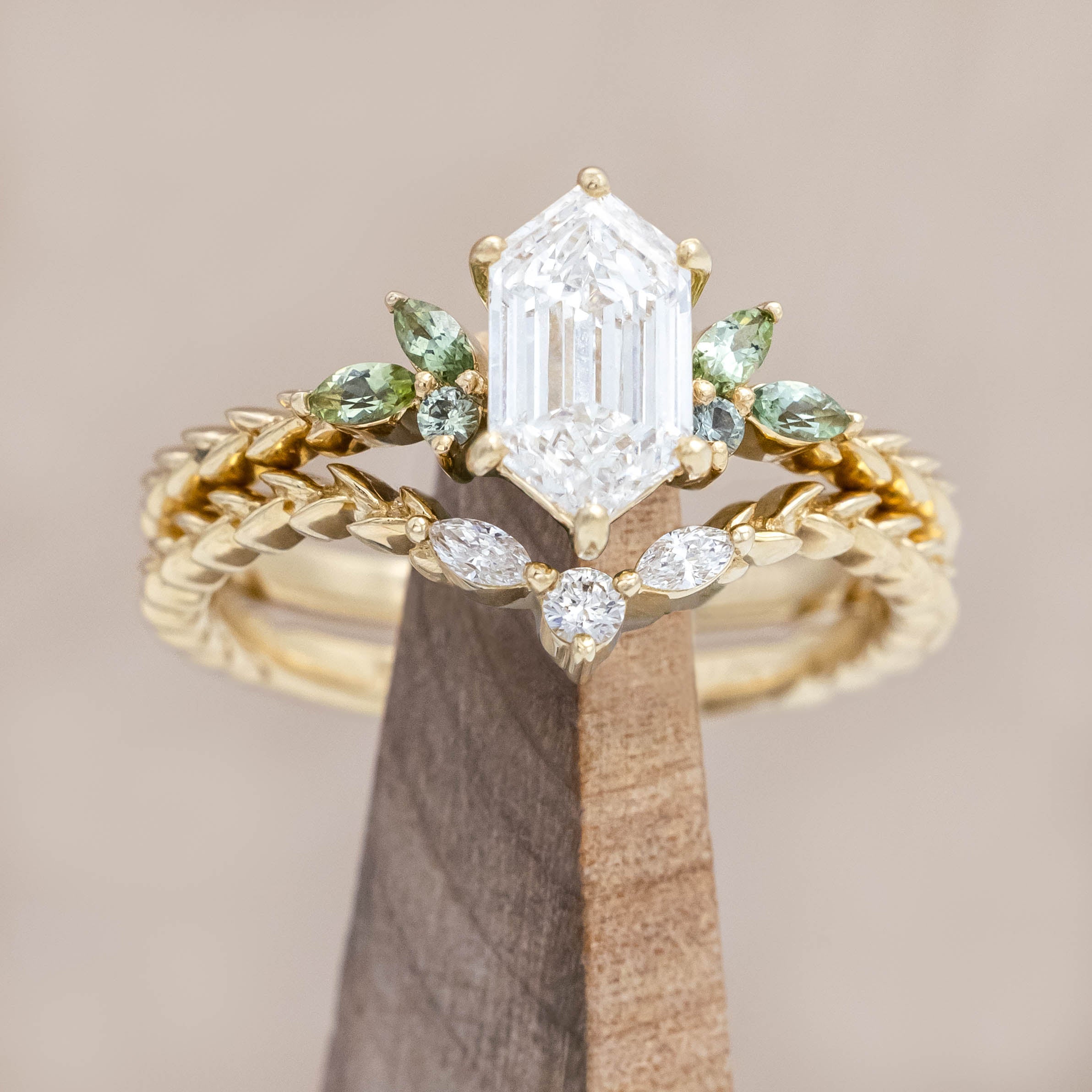 14K gold ring with diamond center stone featuring green sapphire and tourmaline accents on a wooden stand against a beige background