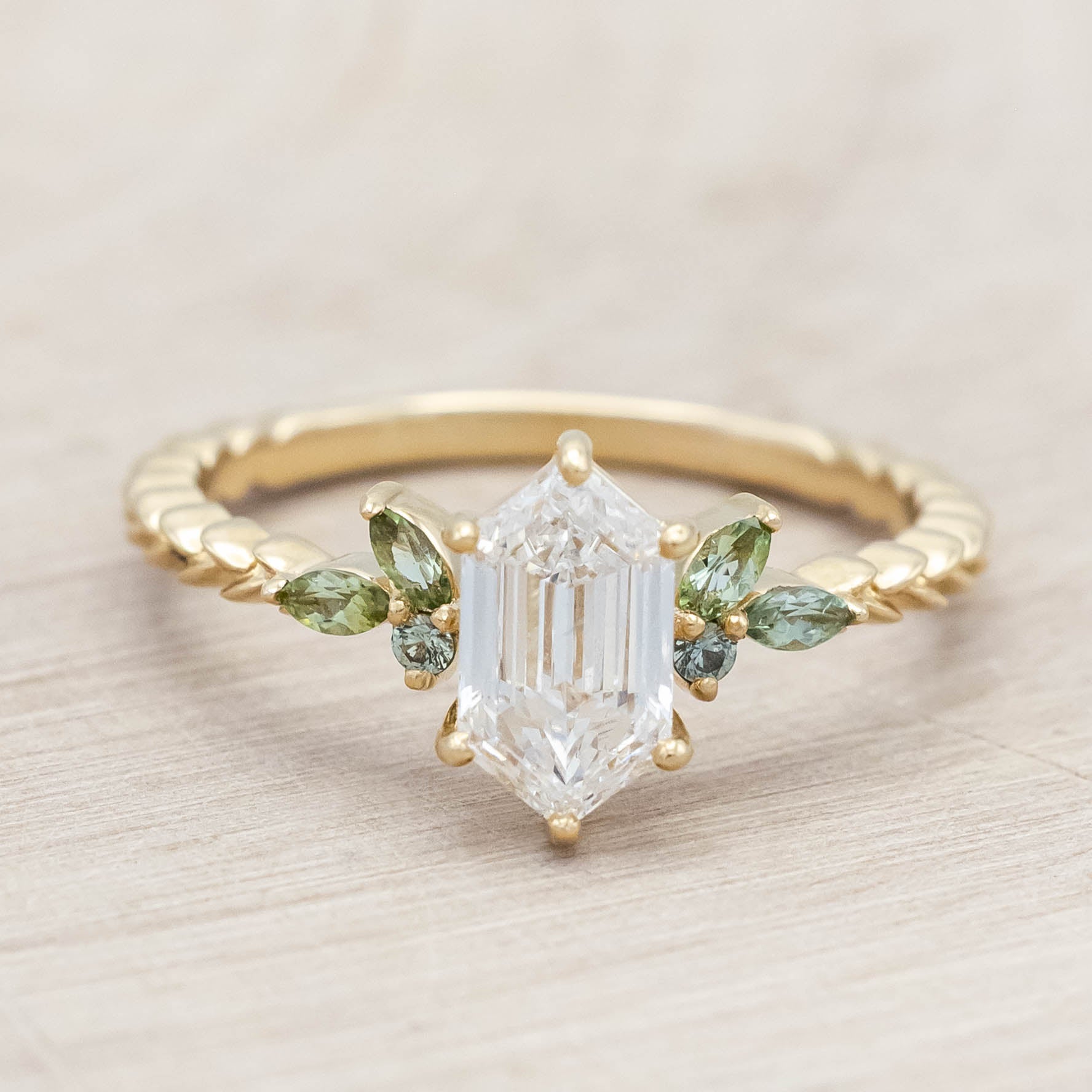 14K gold ring with diamond center stone featuring green sapphire and tourmaline accents on a light wooden background