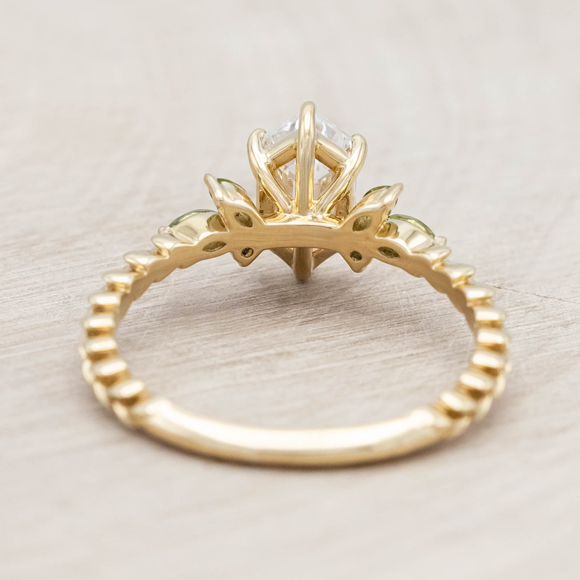 14K gold ring with diamond center stone featuring green sapphire and tourmaline accents on a light wooden background