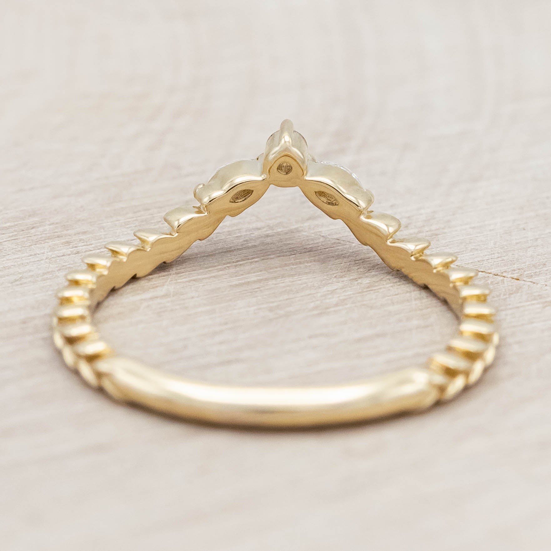 14K gold ring with three diamonds on a wooden stand against a beige background