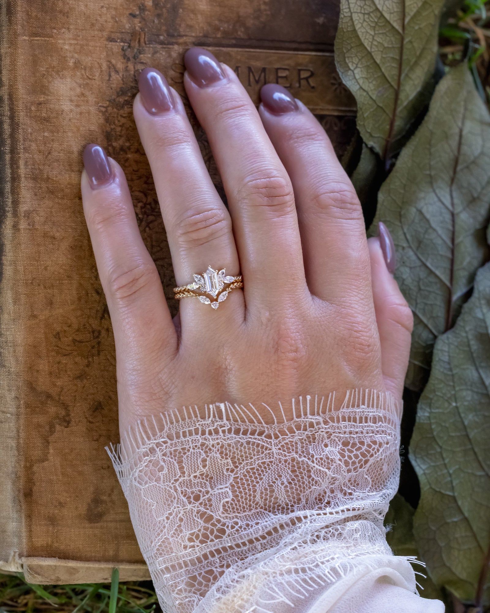 Hand wearing a gold ring with a diamond on a textured surface with leaves.
