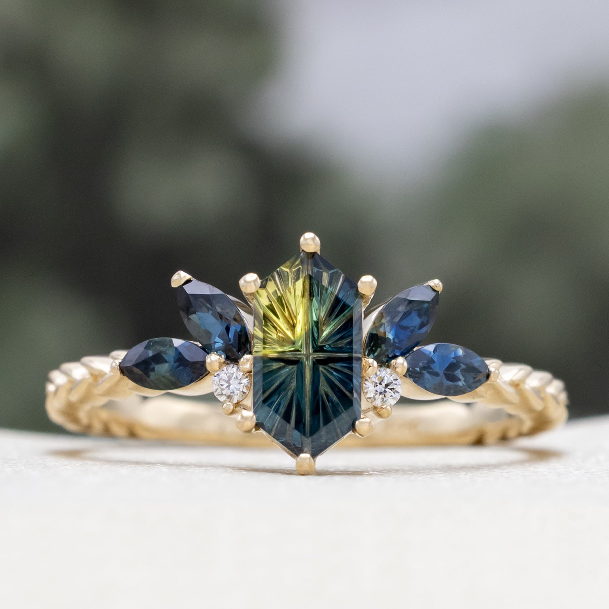 Gold ring with Australian sapphire center stone and diamond accents on a blurred background