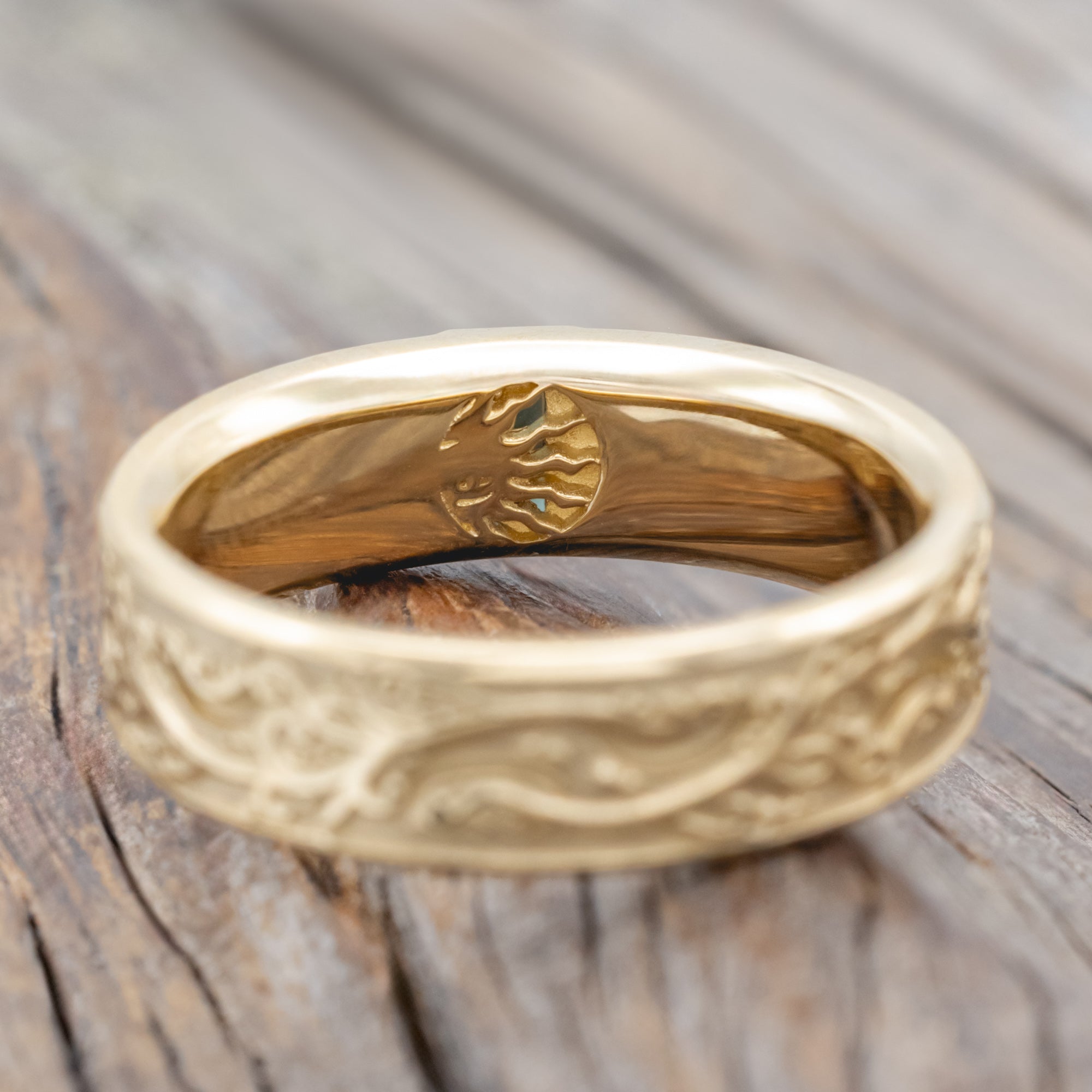 A gold ring with intricate floral engravings and a blue-green sapphire resting on a wooden surface.