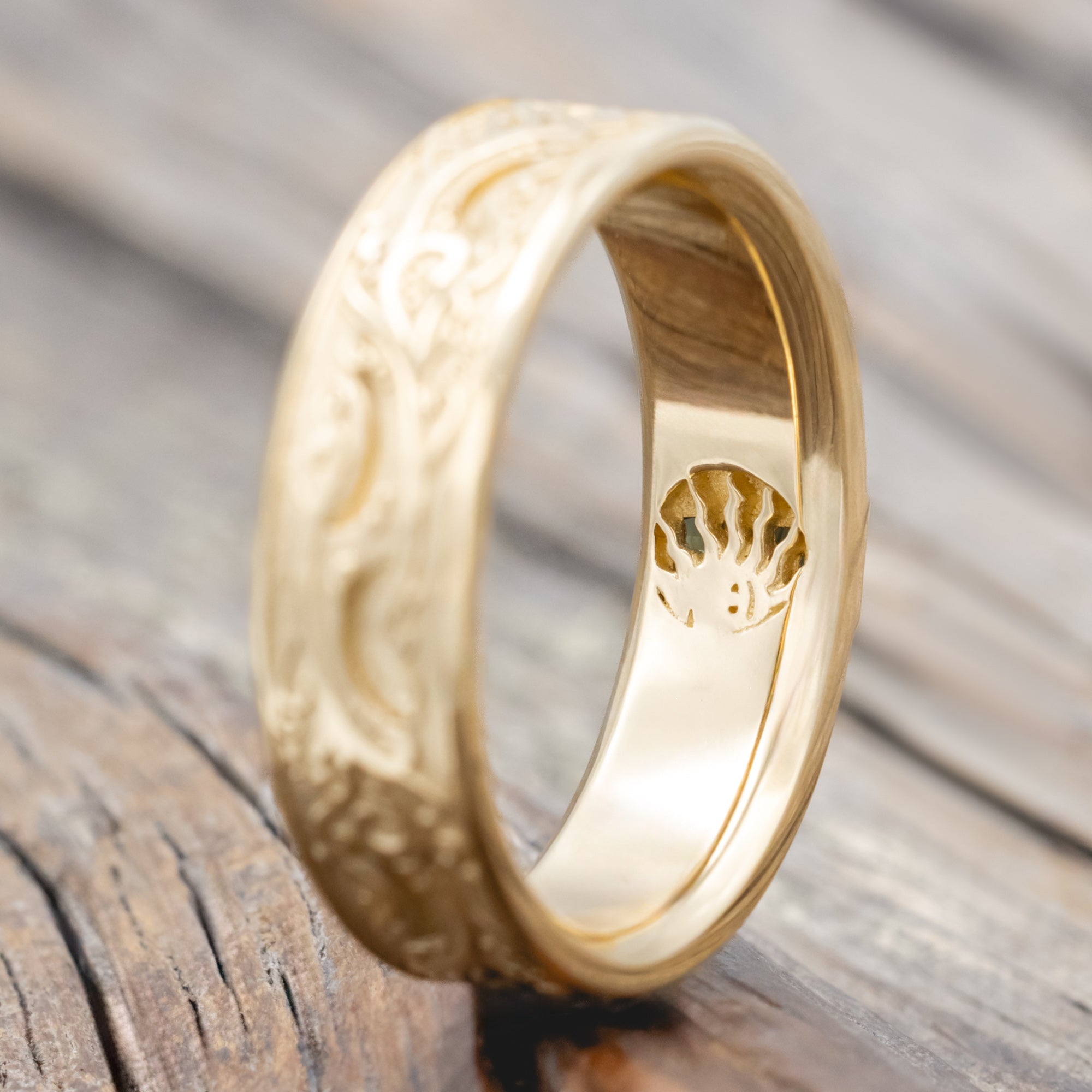 A gold ring with intricate floral engravings and a blue-green sapphire resting on a wooden surface.