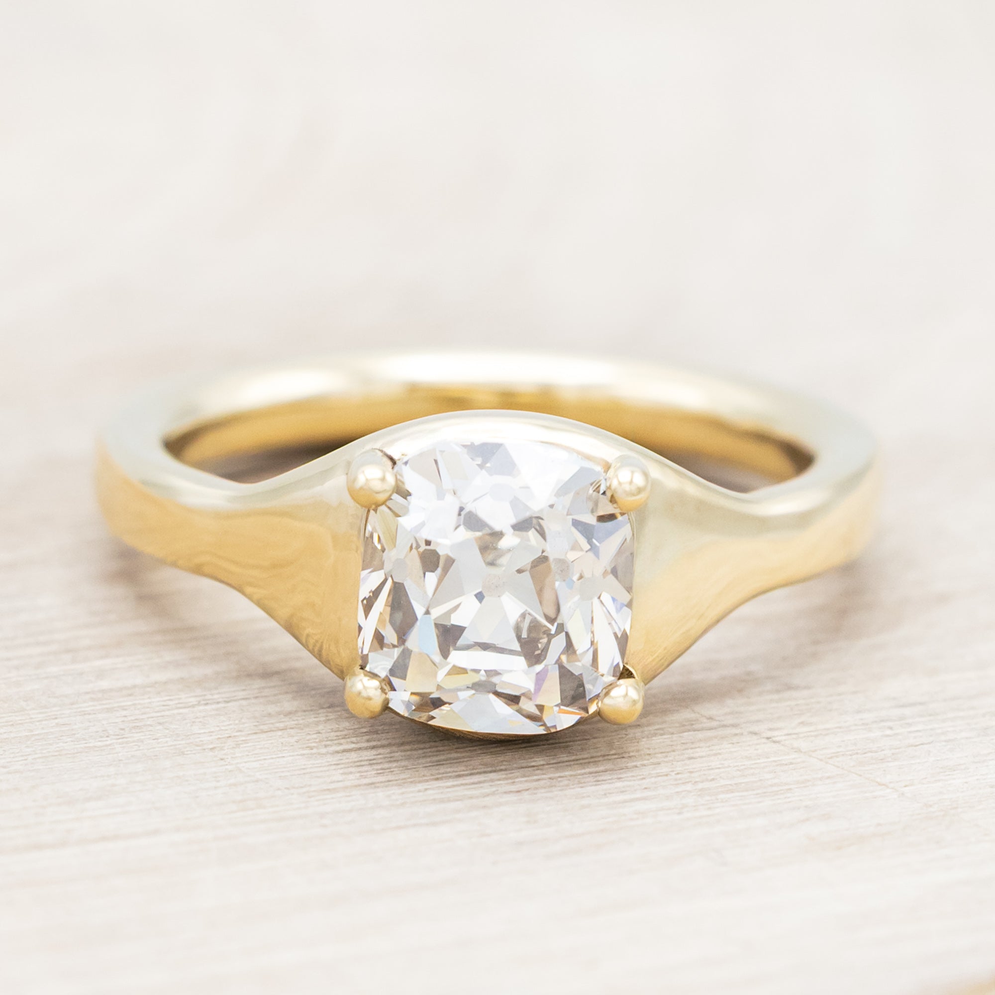 Gold ring with a large salt & pepper diamond on a light wooden surface