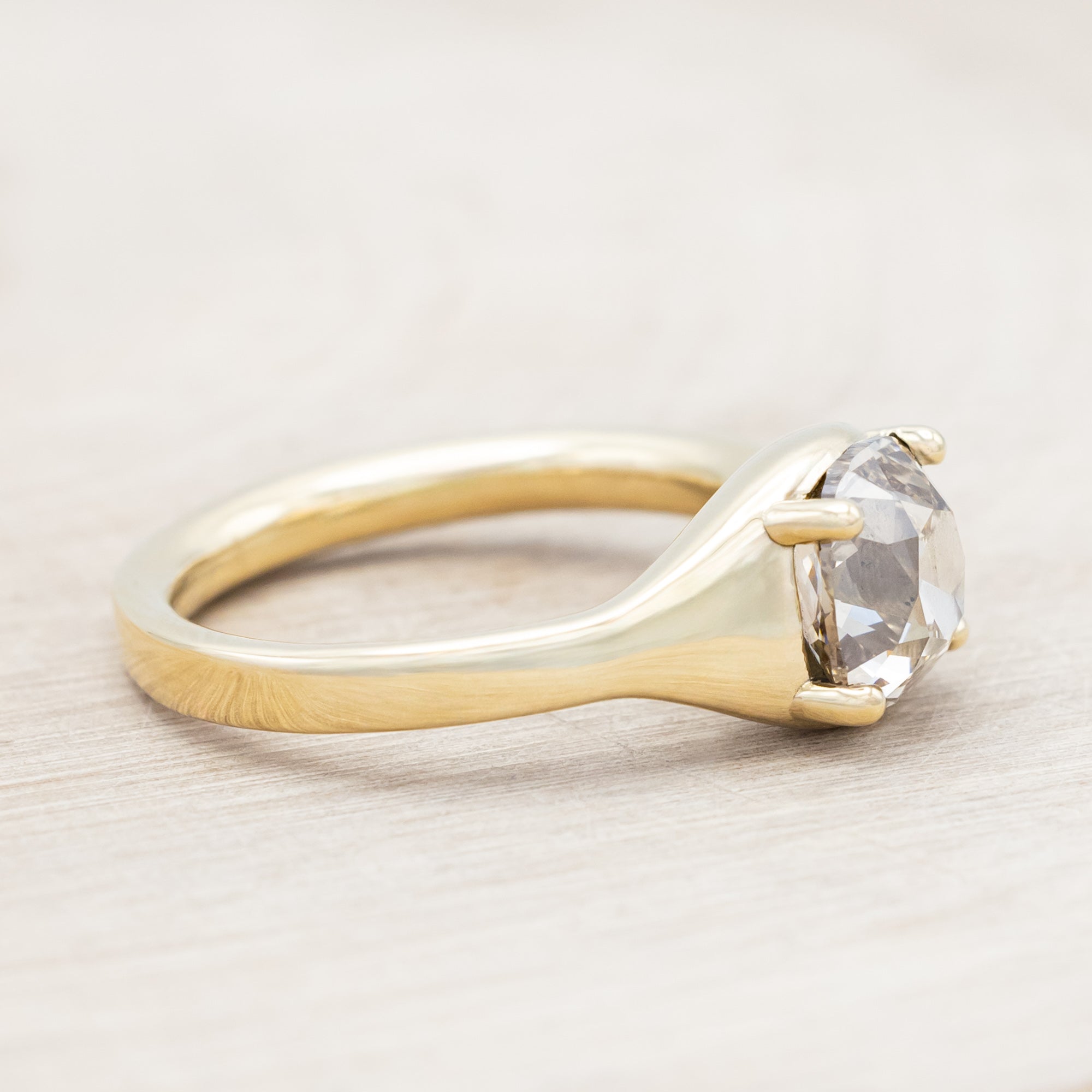 Gold ring with a large salt & pepper diamond on a light wooden surface