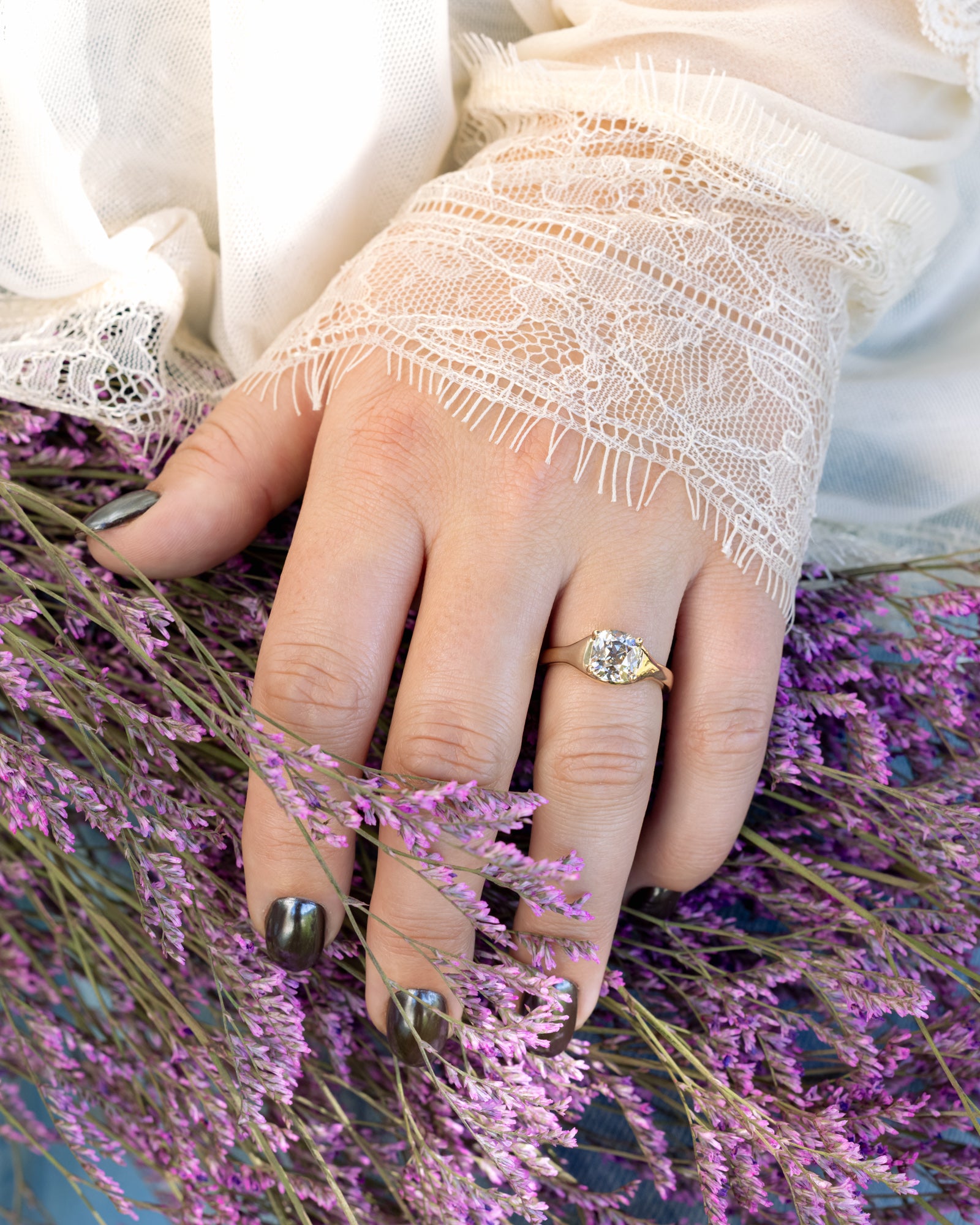 Hand wearing a gold ring with a salt & pepper diamond on a background of purple flowers