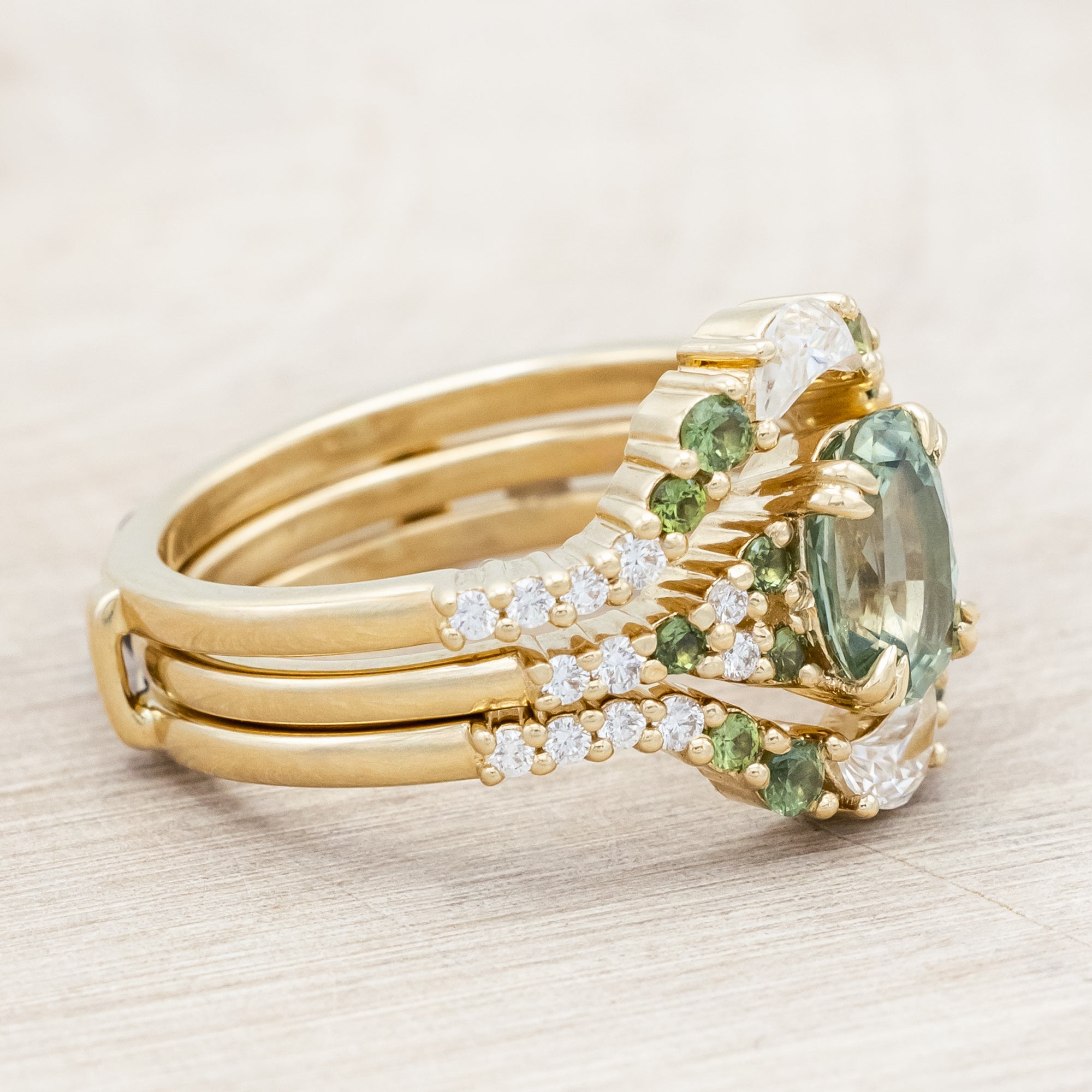 Gold ring with green sapphire and diamond accents on a light wooden surface