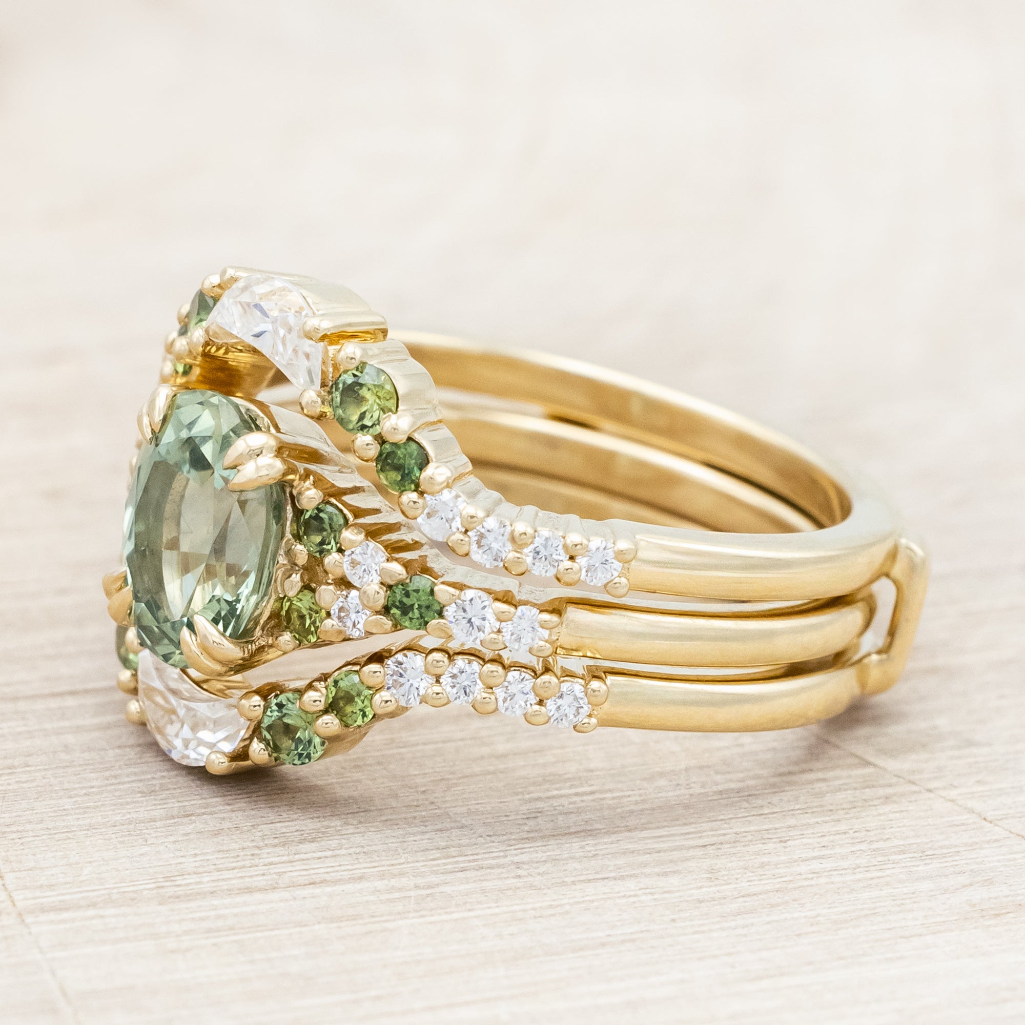 Gold ring with green sapphire and diamond accents on a light wooden surface