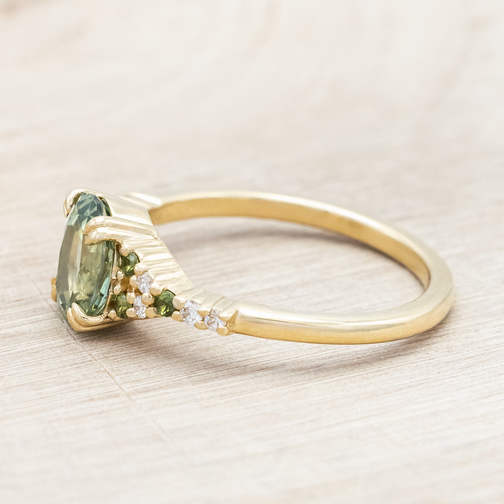 Gold ring with green sapphire and diamond accents on a light wooden surface