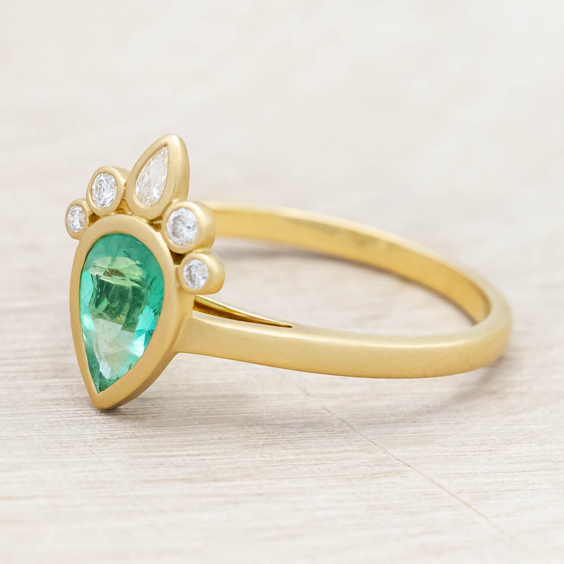 Gold ring with a green emerald and small diamonds on light wooden background