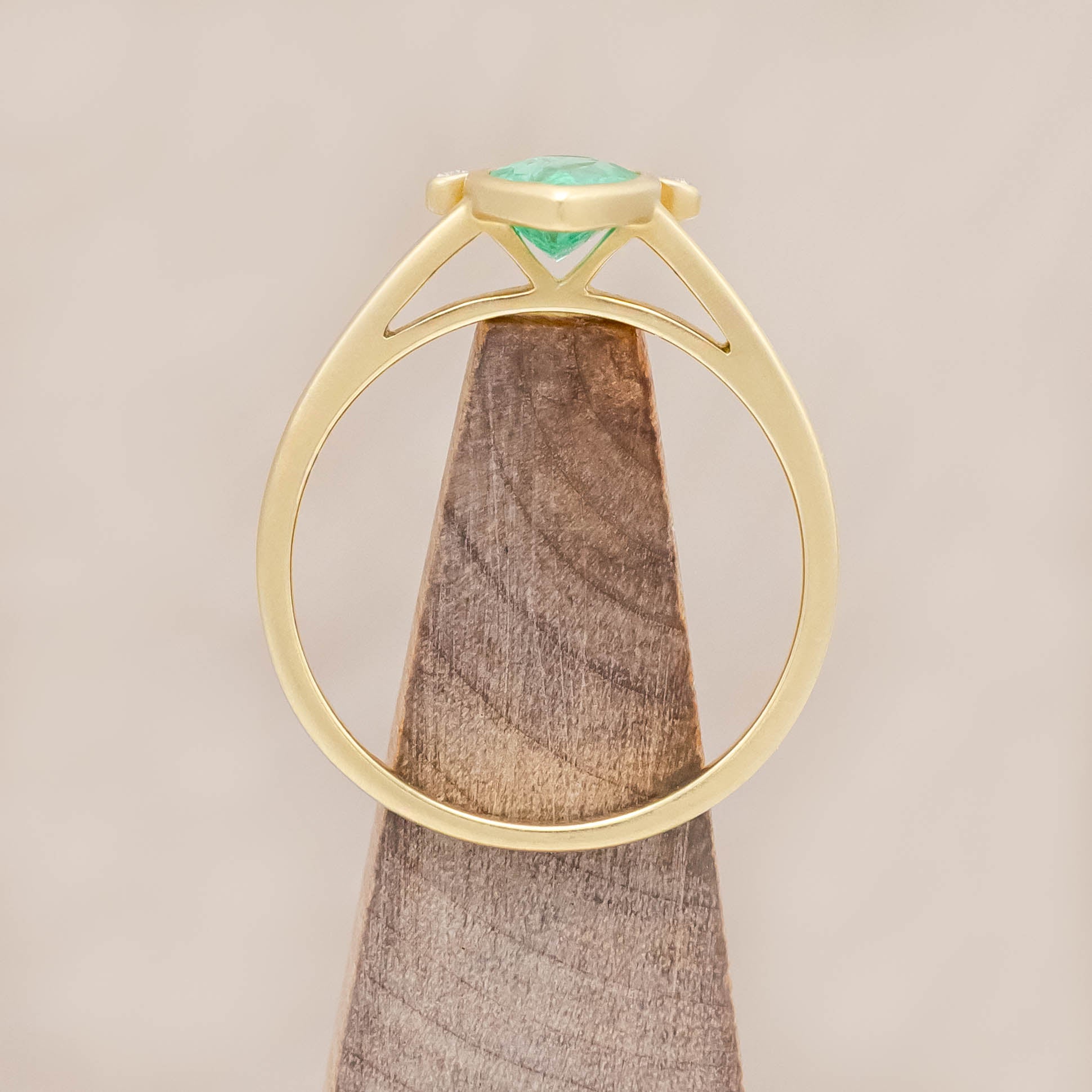 Gold ring with a green emerald and small diamonds on a wooden stand against beige background