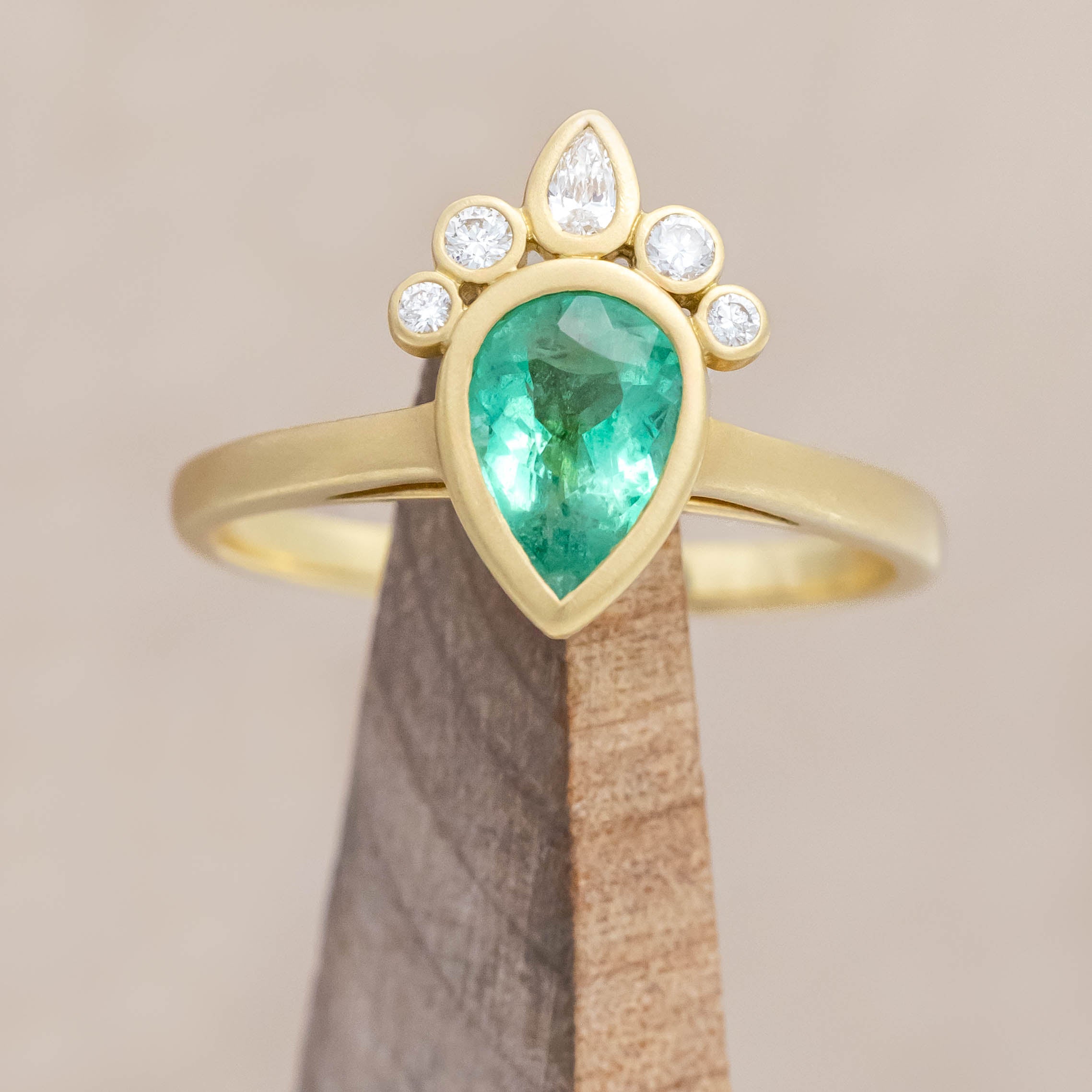 Gold ring with a green emerald and small diamonds on a beige background