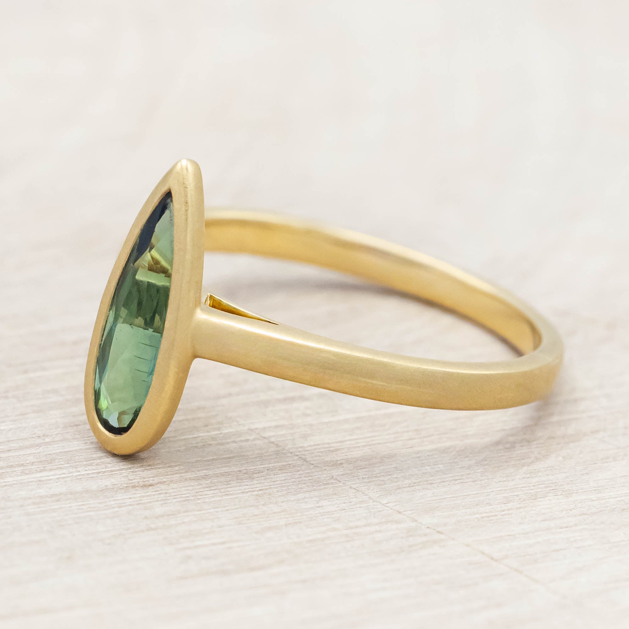 Gold ring with a green tourmaline gemstone on a light wooden surface