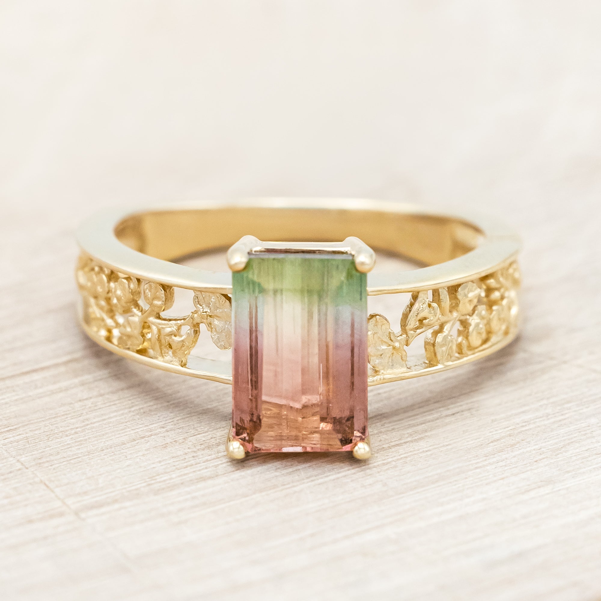 14K gold ring with a green and pink gemstone on a beige background