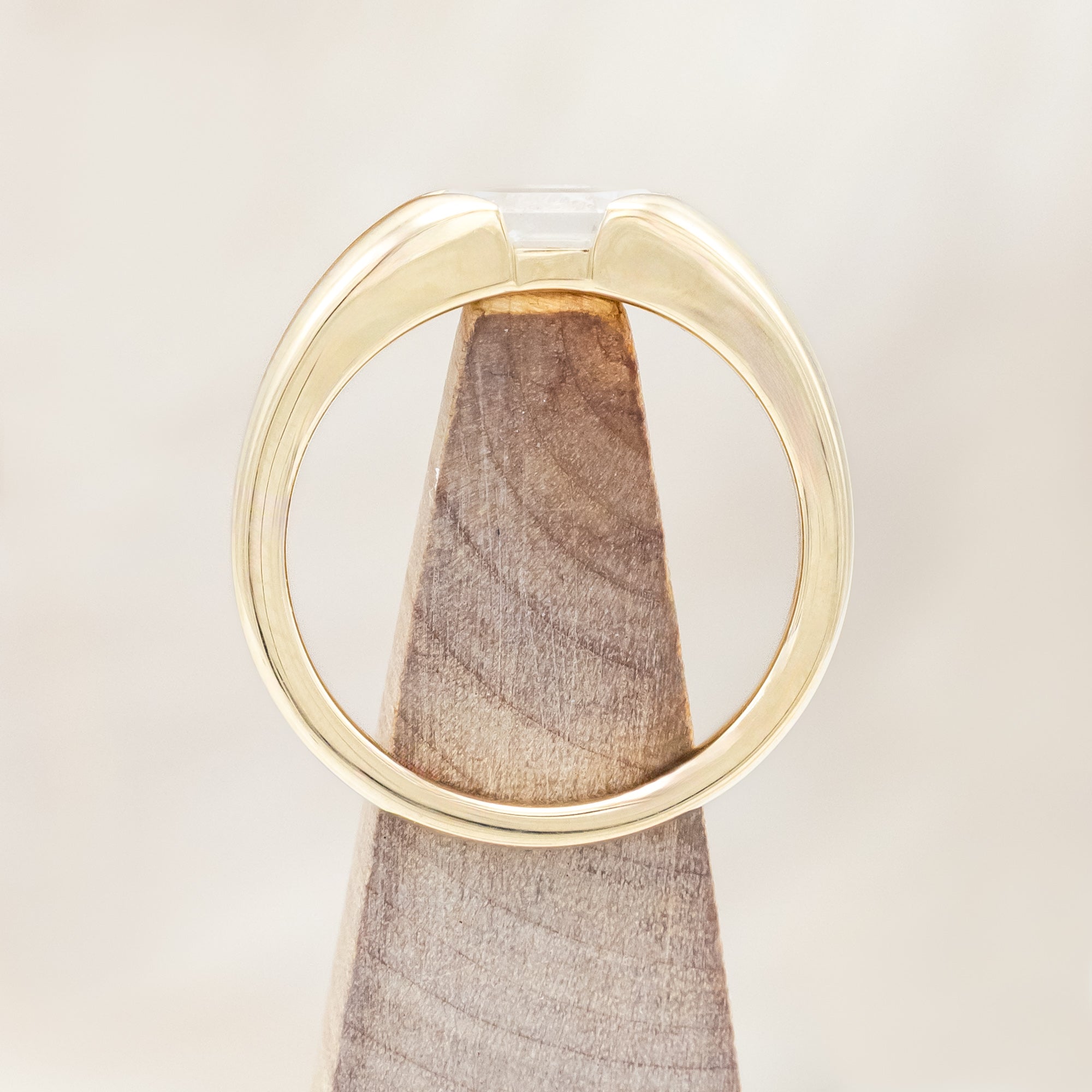 14K gold ring with a geometric stone on a wooden stand against a beige background