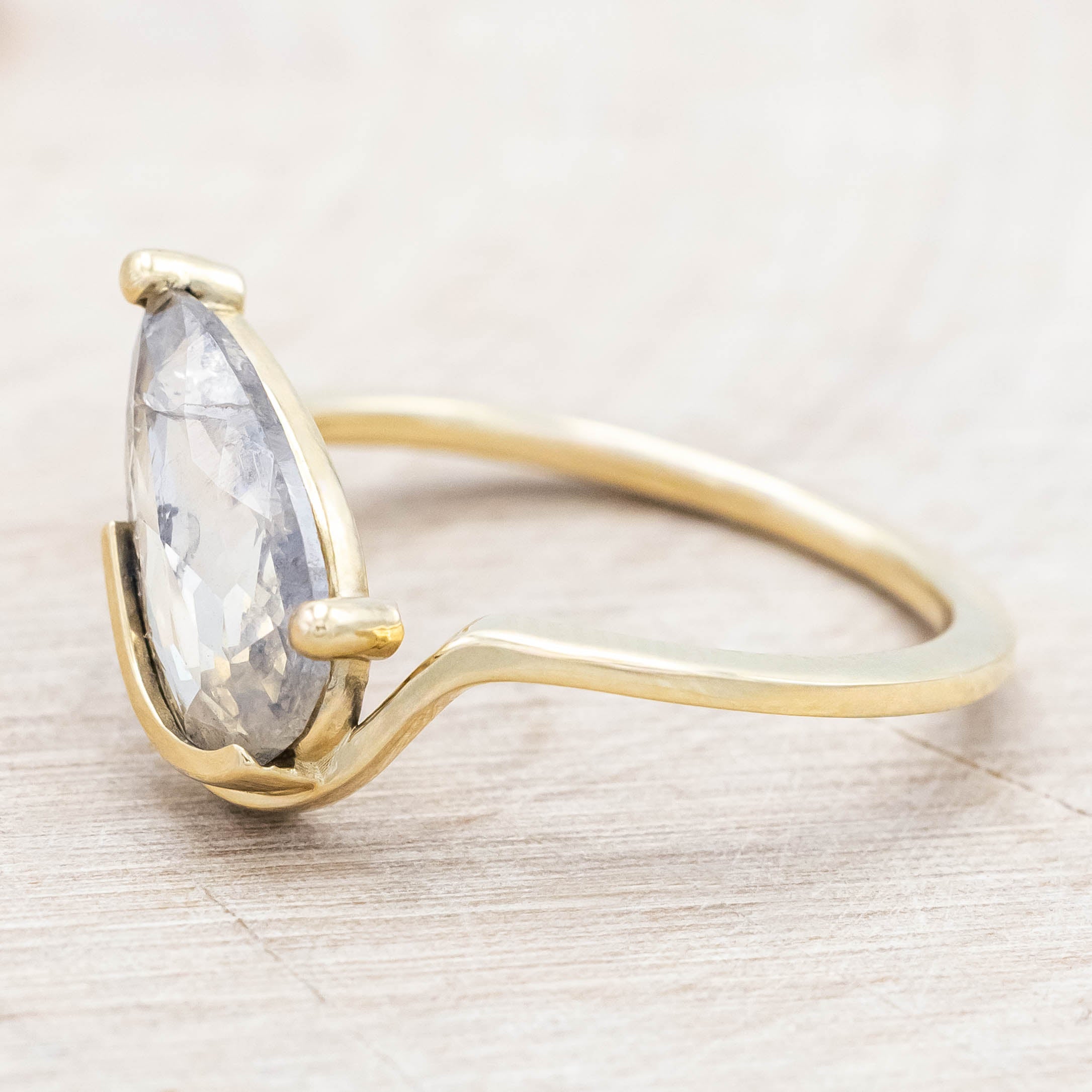 Gold ring with a salt & pepper diamond on a light wooden background