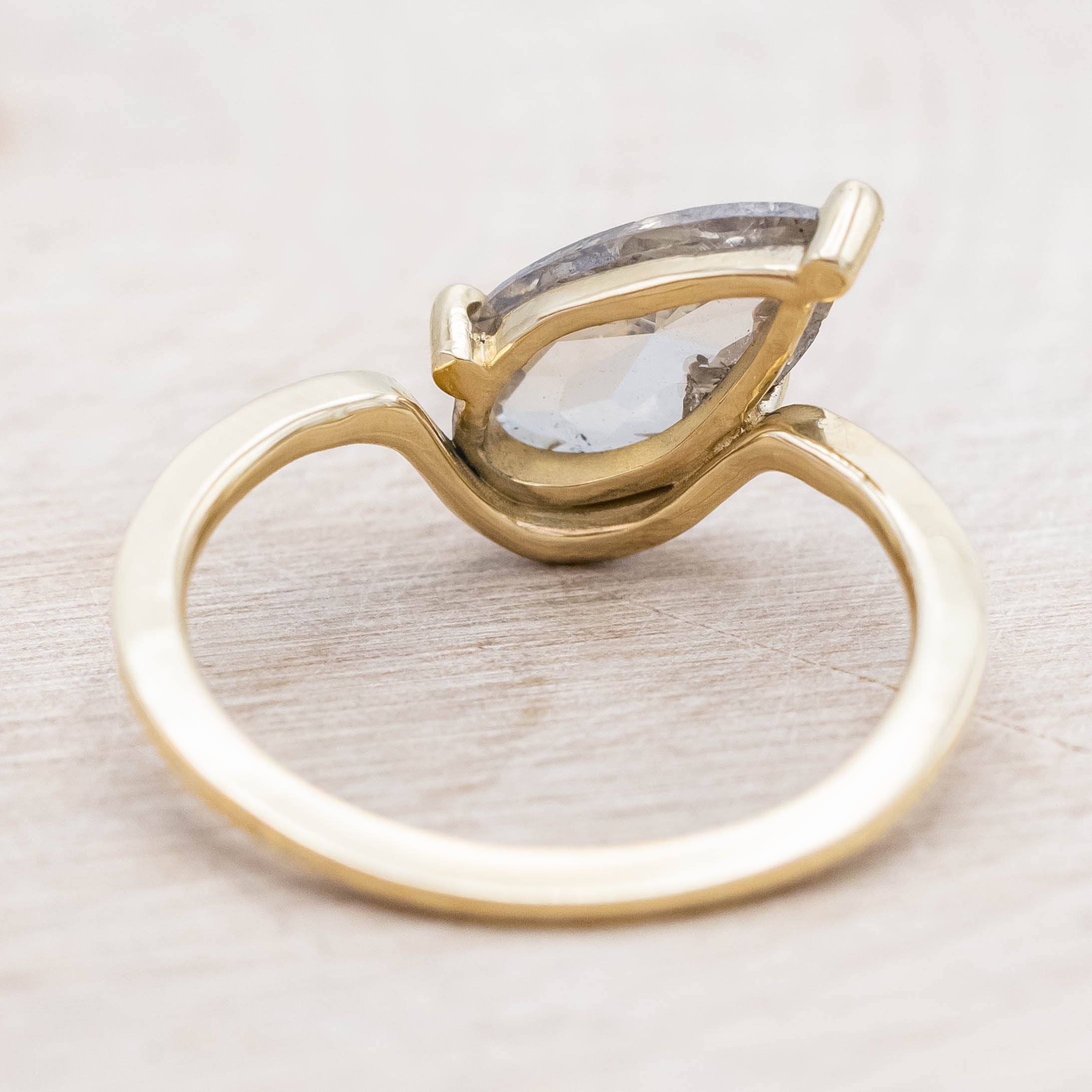Gold ring with a salt & pepper diamond on a light wooden background