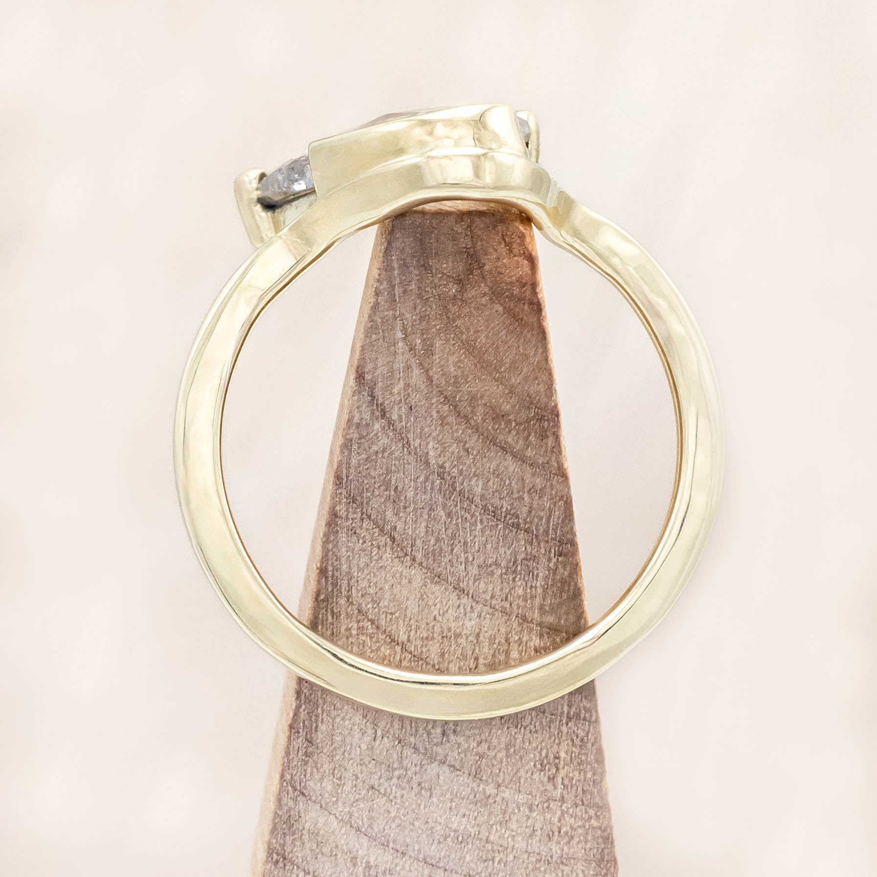 Gold ring with a salt & pepper diamond on a wooden stand against a beige background