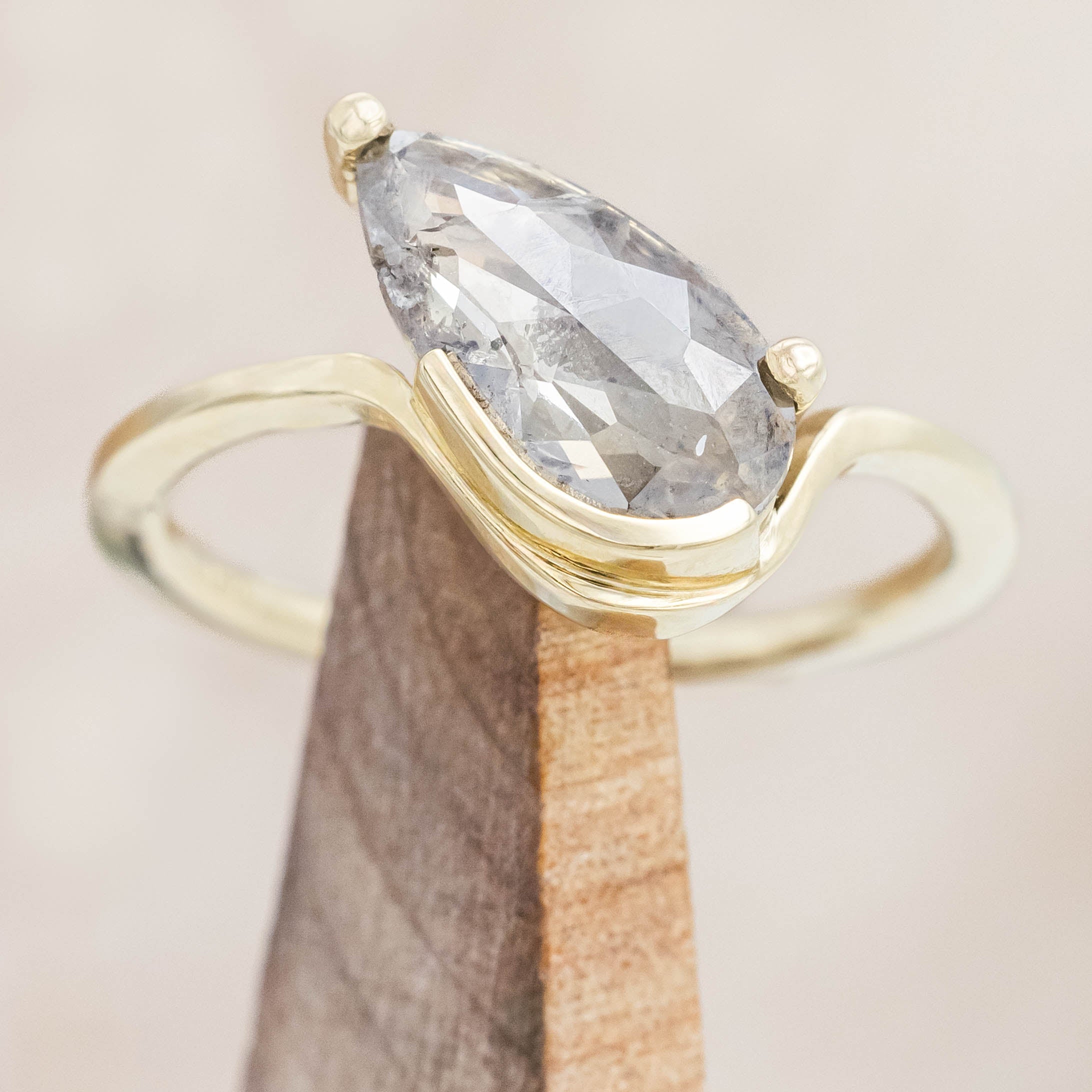 Gold ring with a salt & pepper diamond on a wooden stand against a neutral background