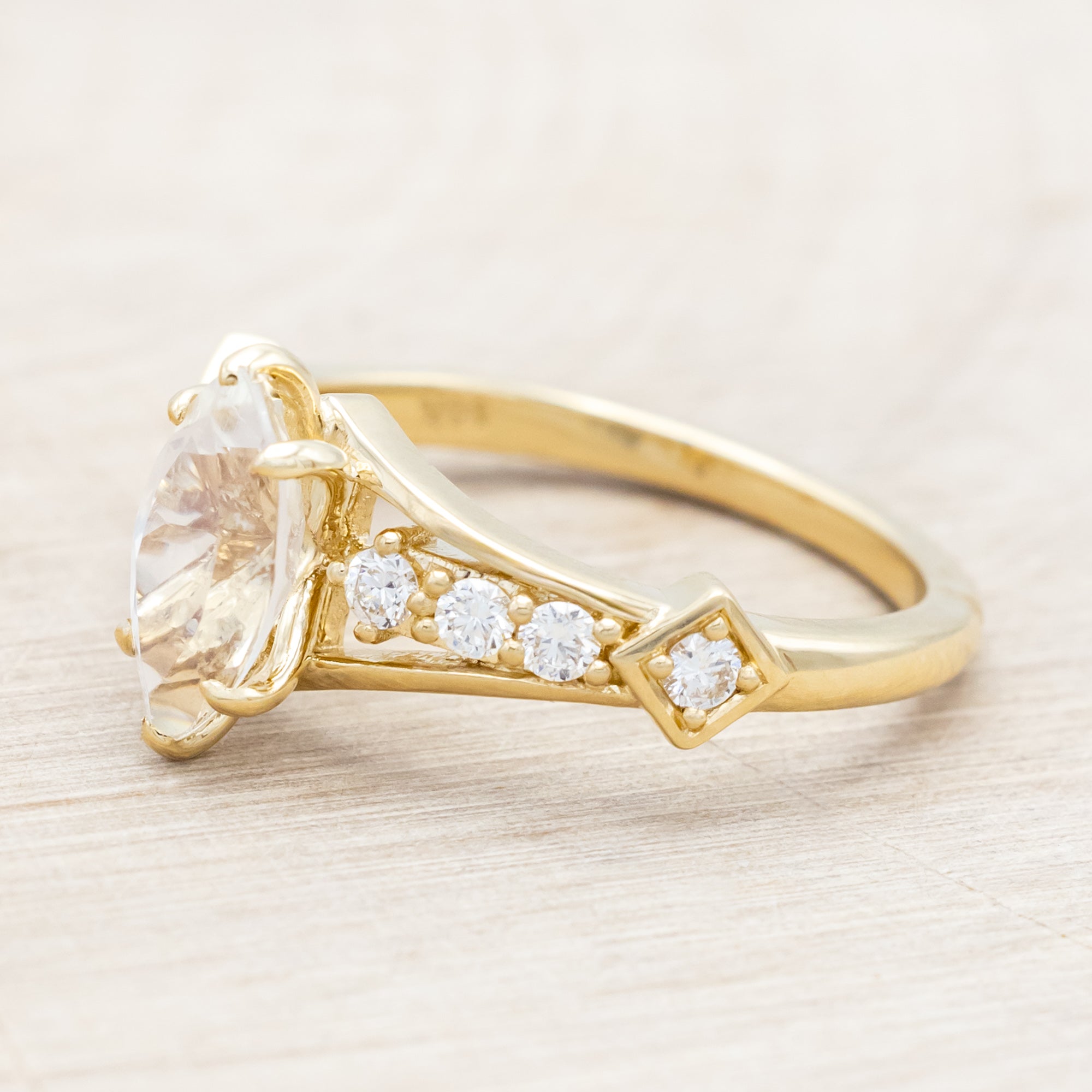 Yellow gold ring with a moonstone and smaller diamonds on a beige background