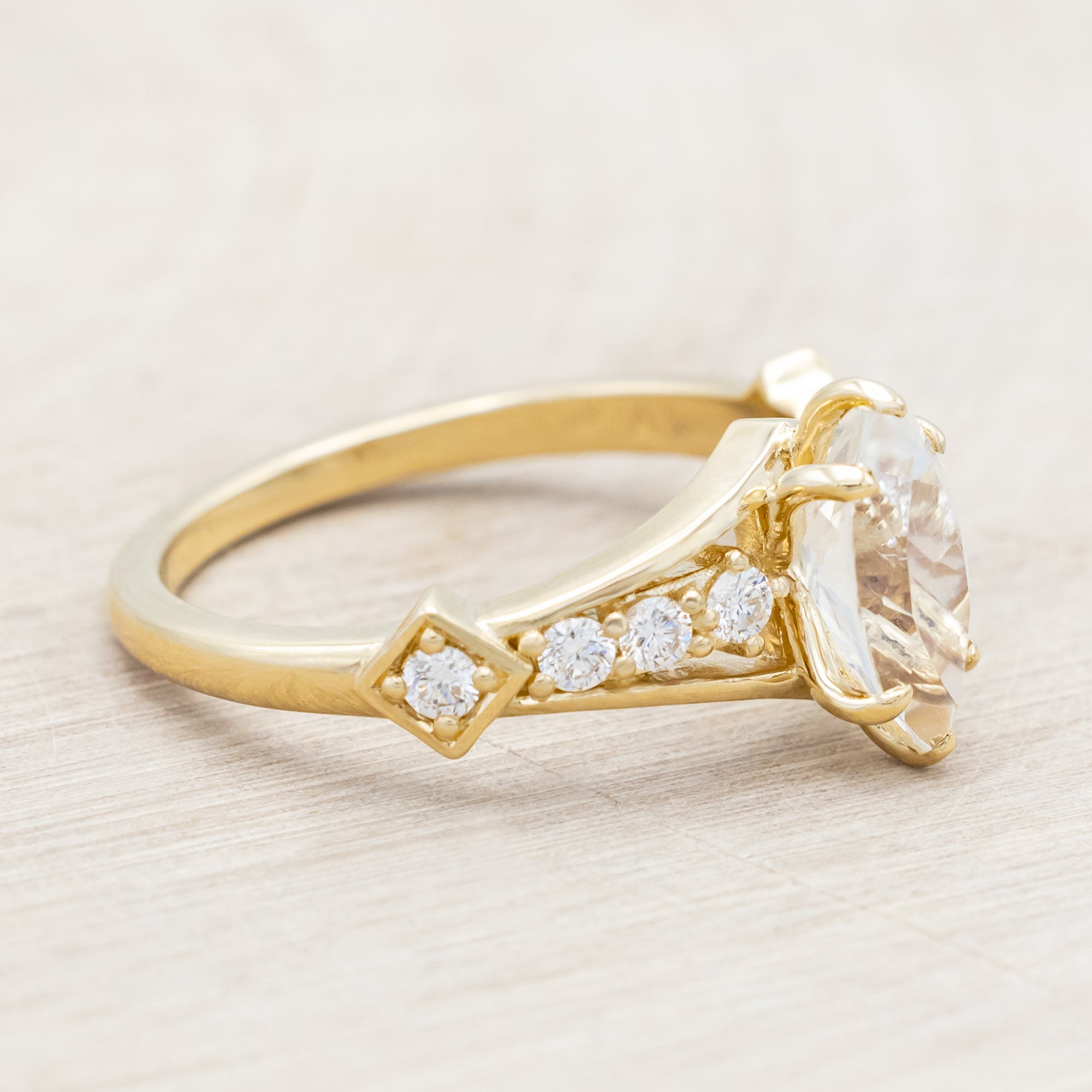 Yellow gold ring with a moonstone and smaller diamonds on a beige background