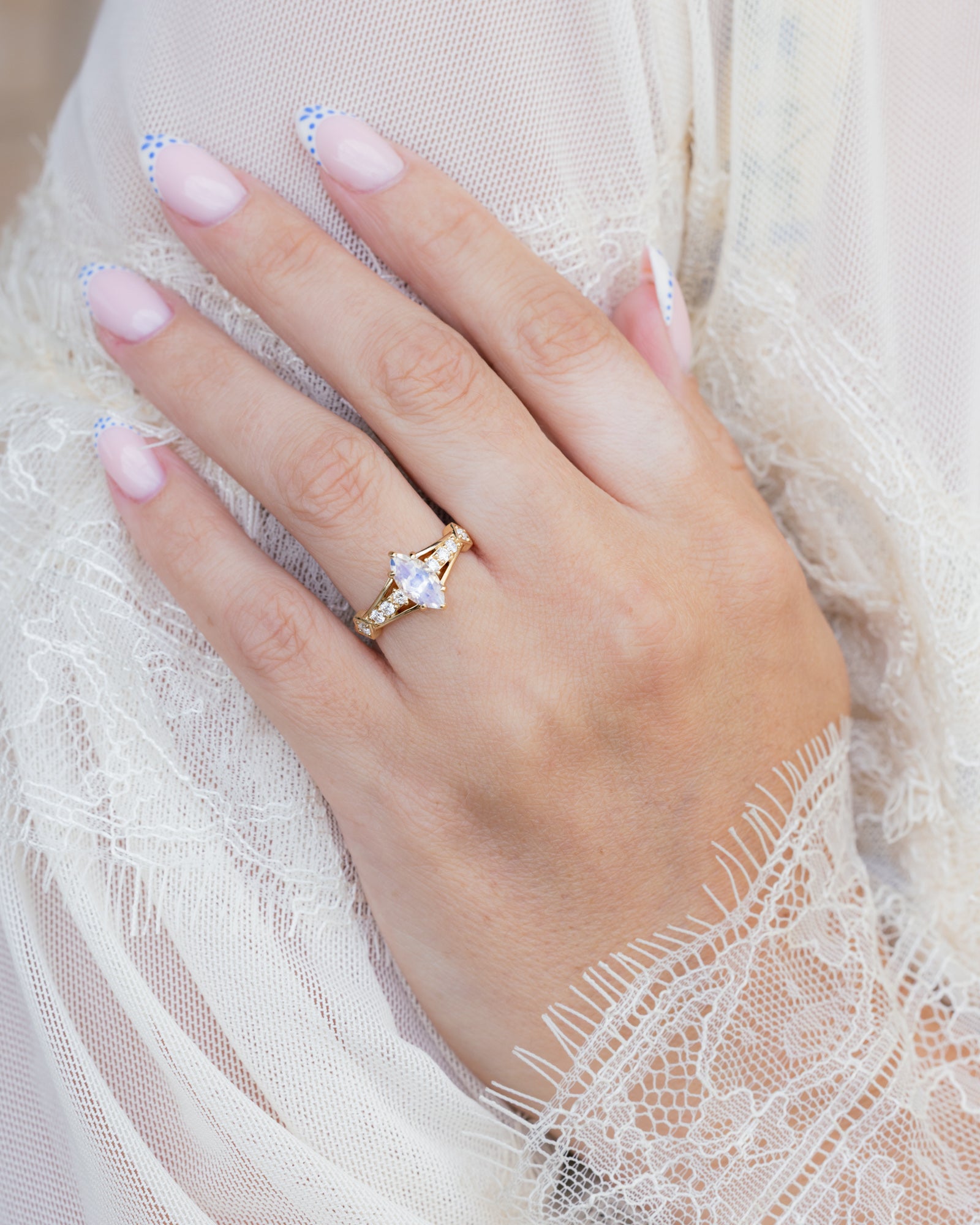 Hand wearing a gold ring with moonstone against a lace background