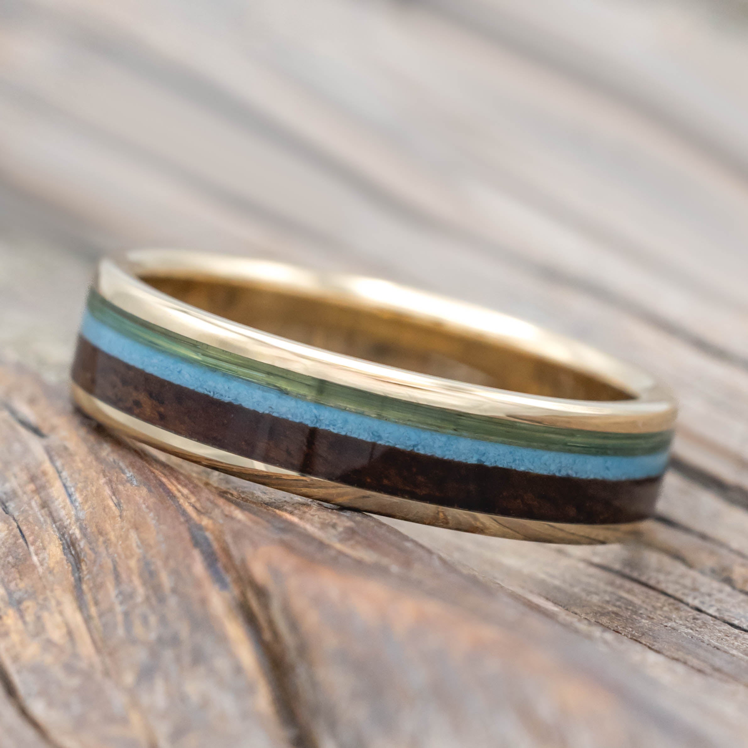 Yellow gold ring with fishing line, koa wood, and turquoise inlays on a wooden surface